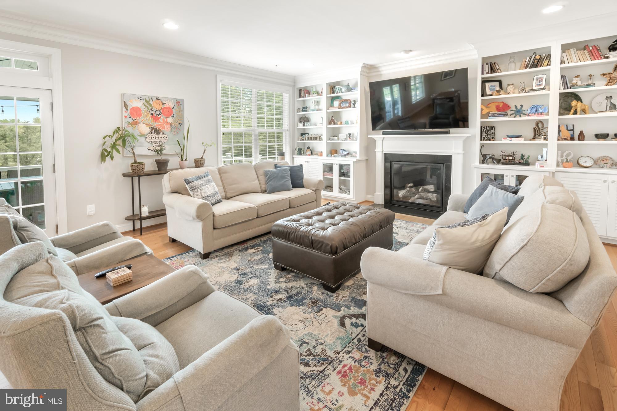 Living room with beige seating, a tufted leather ottoman, and white built-in shelves around the fireplace.