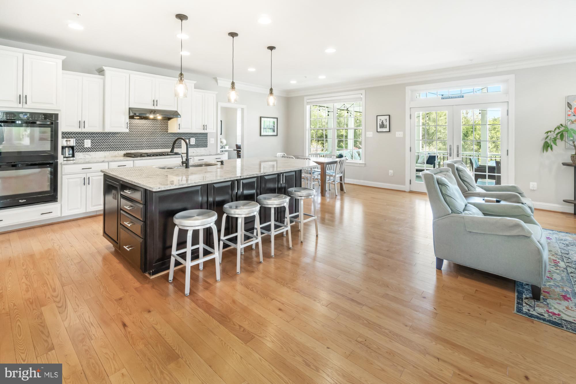 Open kitchen and living area with a dark island, white cabinets, hardwood floors, and French doors.