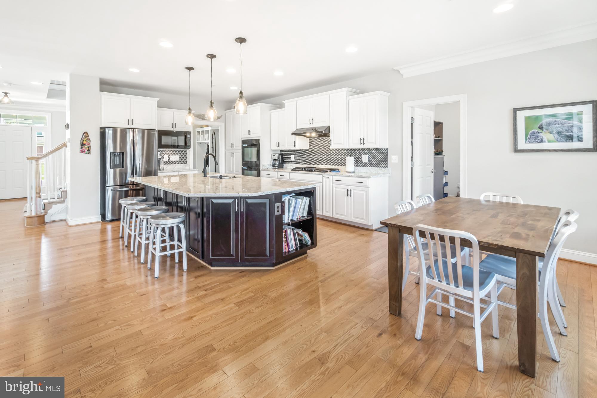 Kitchen with a dark paneled island, white cabinetry, patterned backsplash, and adjoining dining table.