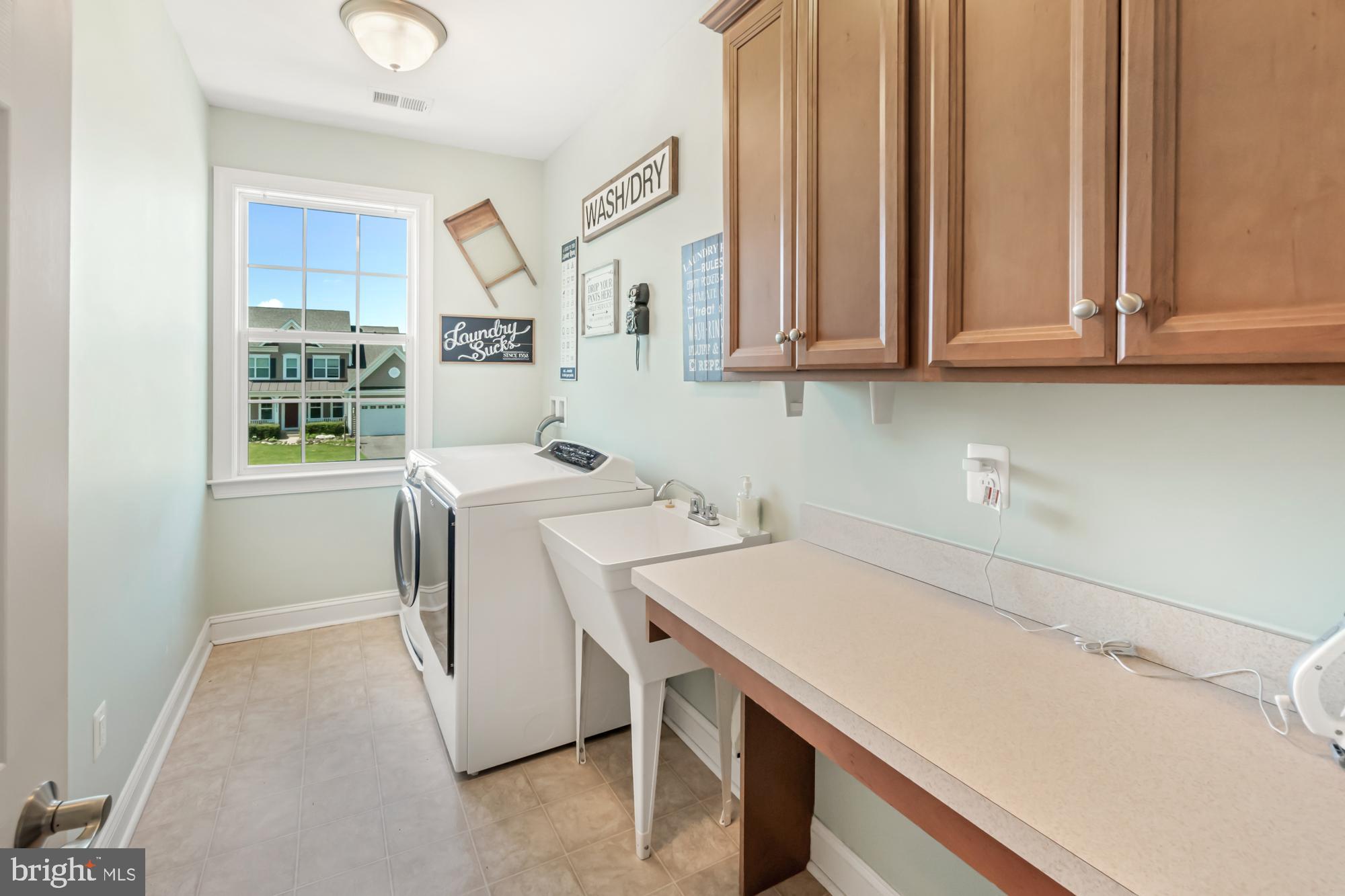Laundry room with washer, dryer, utility sink, long counter, and wood cabinets.