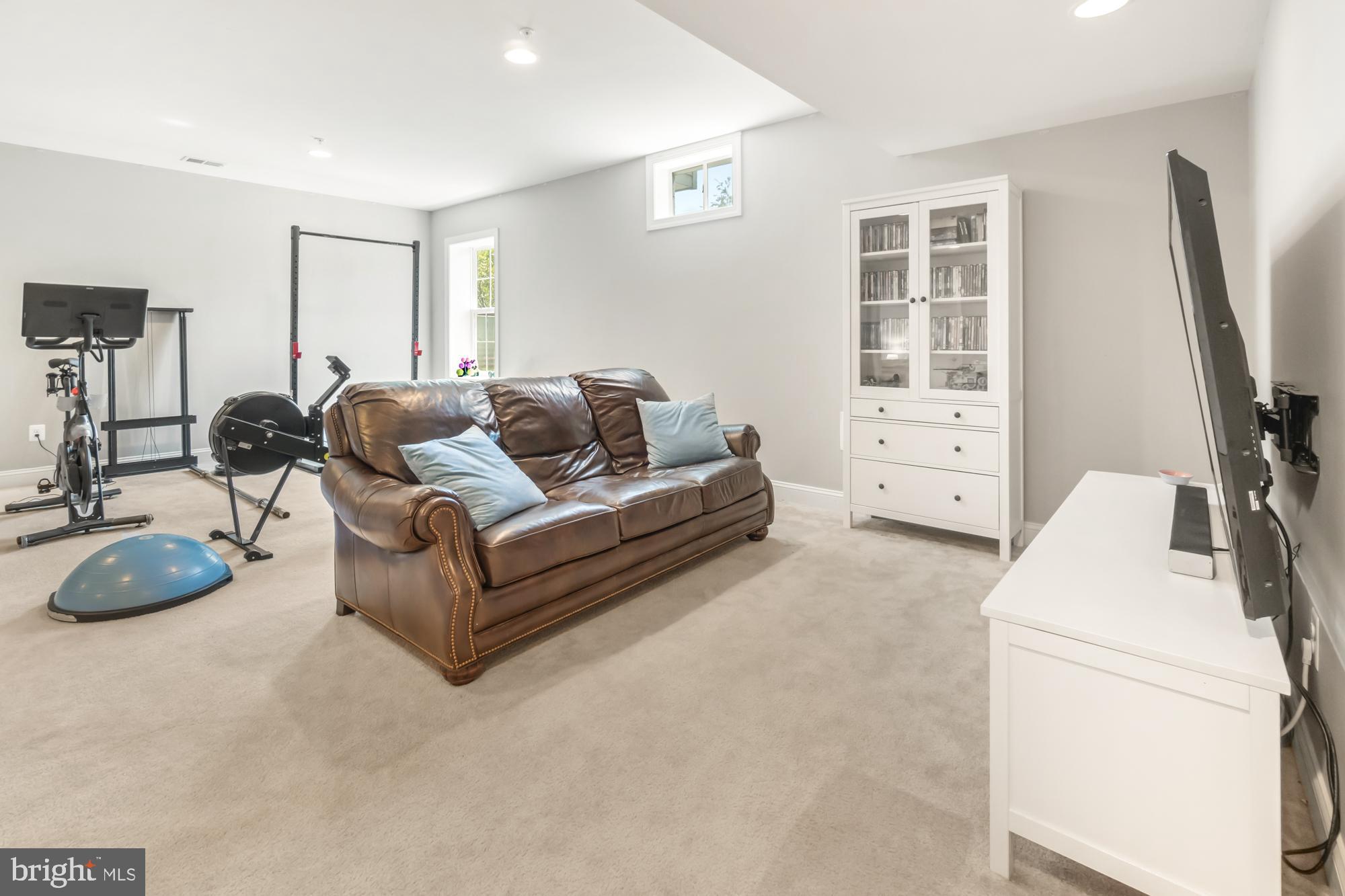 Basement media room with a brown leather sofa, exercise equipment, and a large TV.