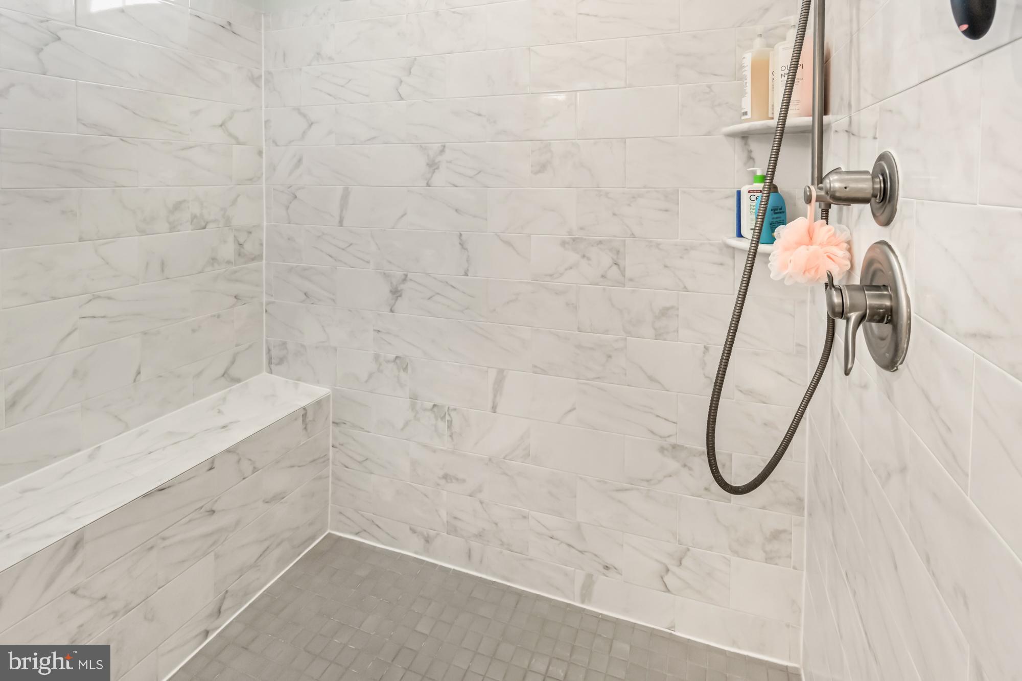 Walk-in shower with marble-look tile, a built-in bench, and brushed metal fixtures.