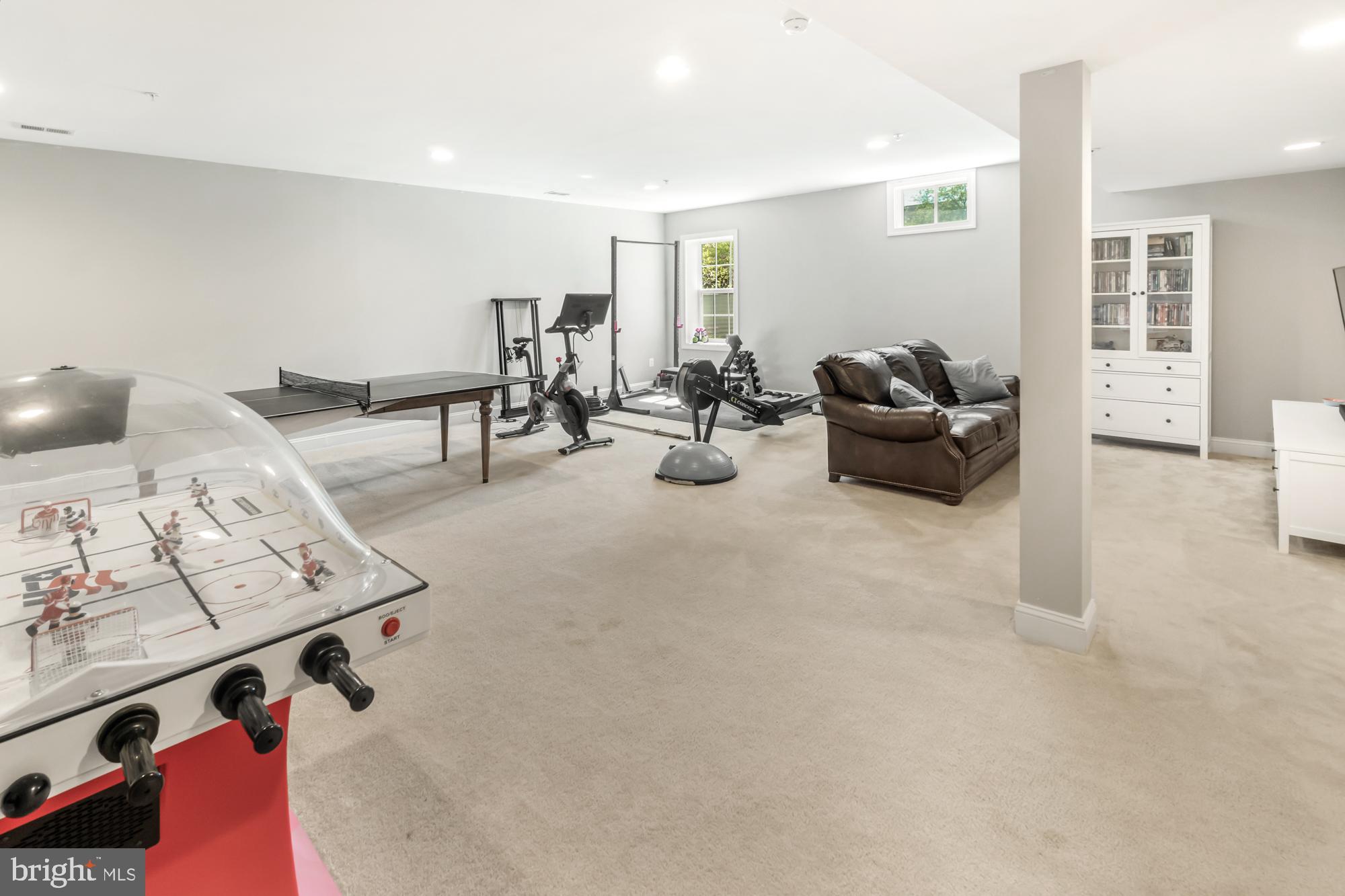 Basement recreation room with foosball and ping-pong tables, workout equipment, and a leather sofa.