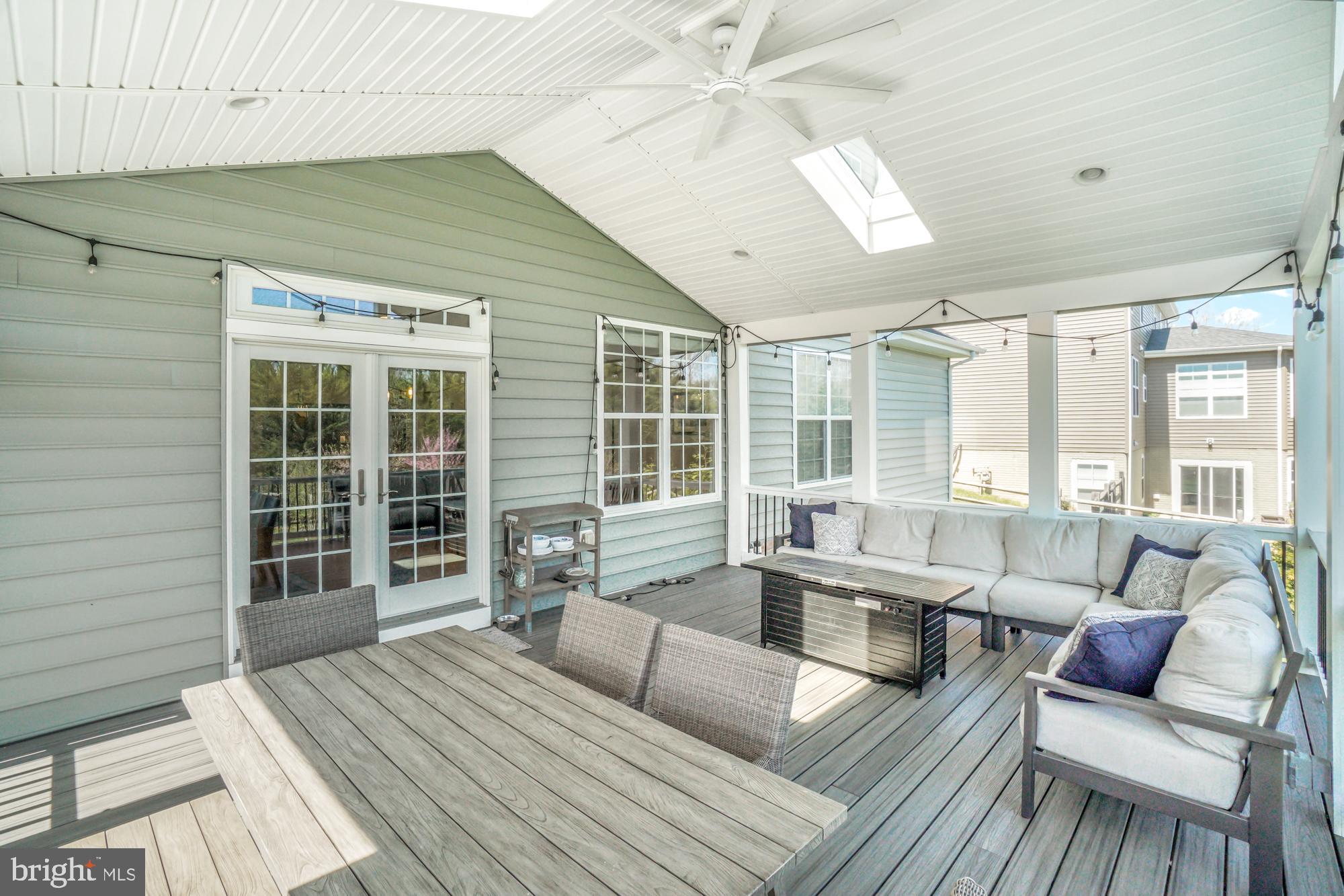 Covered patio with gray decking, dining table, and cushioned sectional beneath a skylit ceiling.