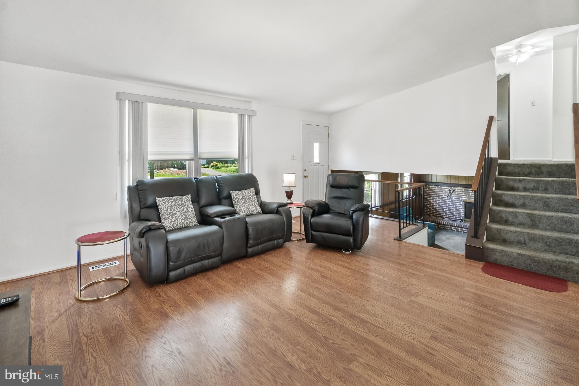Furnished living room with leather seating, wood-look floors, and stairs beside a brick fireplace.