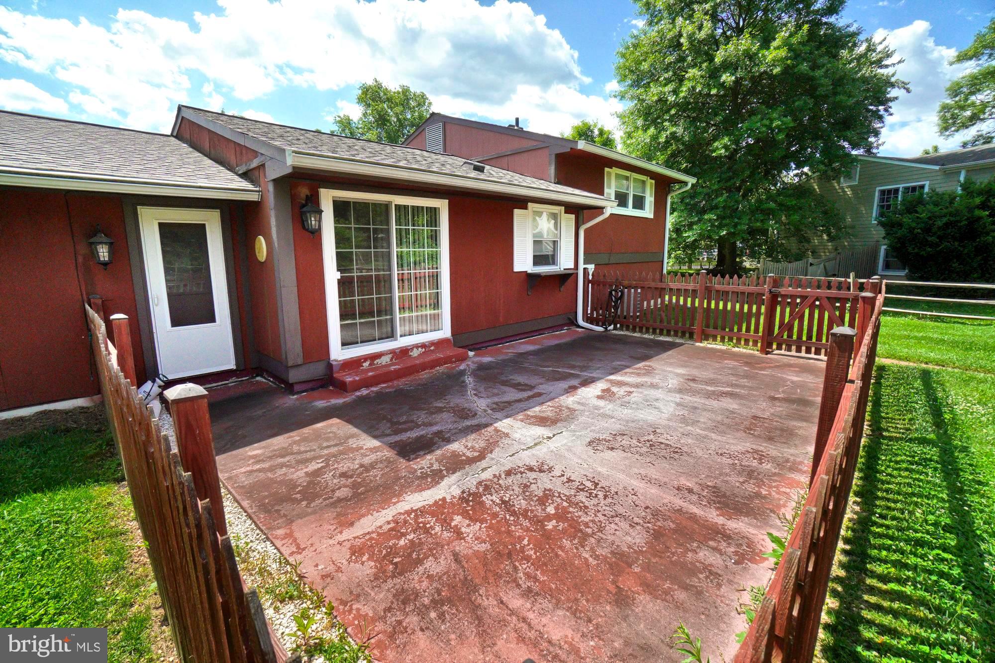 Rear exterior of a red-sided home with a fenced concrete patio and sliding glass door.