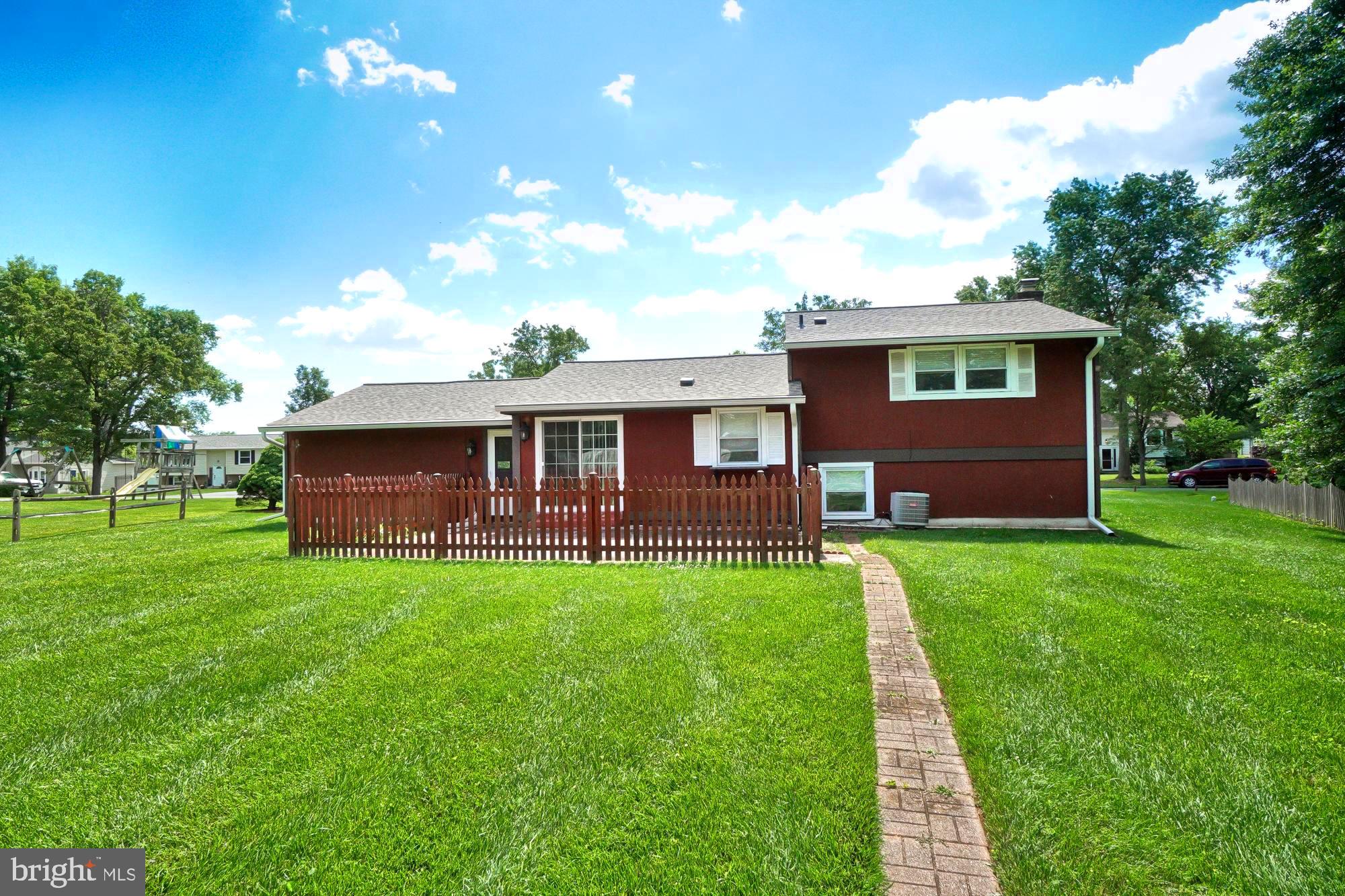 Rear exterior of a red two-story home, with a fenced patio and brick path through a wide lawn.