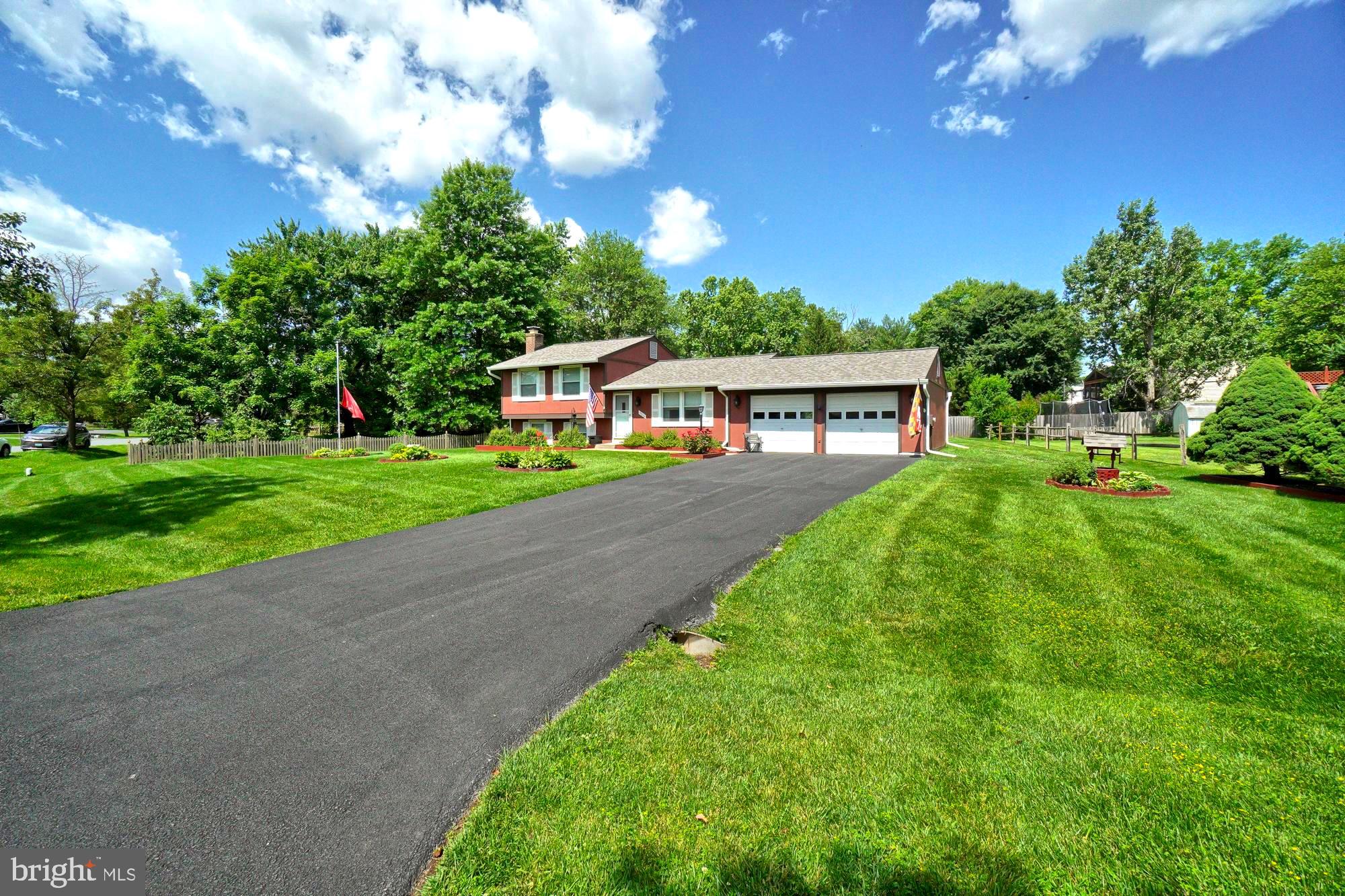 Red split-level home with a two-car garage, long driveway, and landscaped lawn.