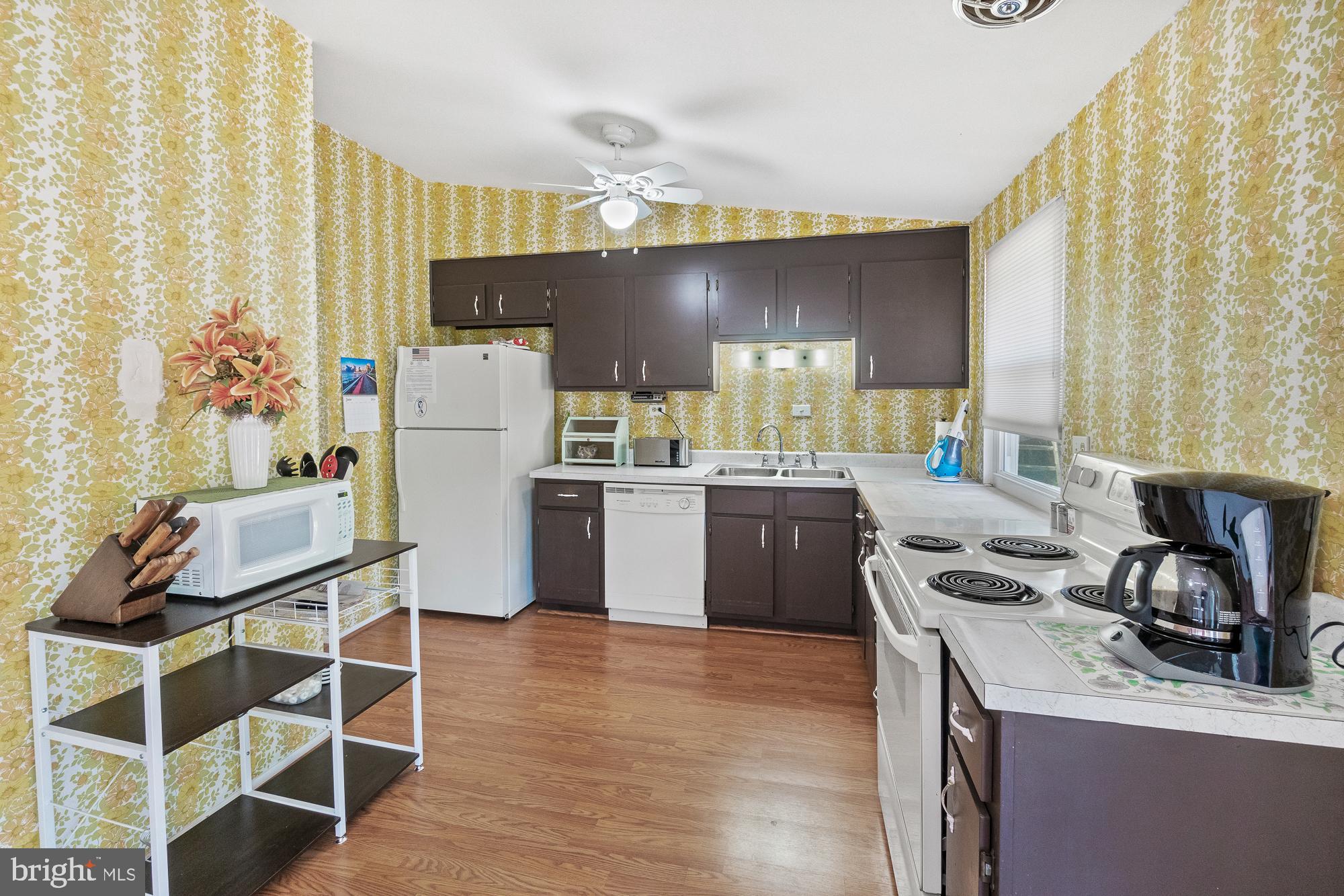 Kitchen with yellow floral wallpaper, dark cabinets, white appliances, and wood flooring.