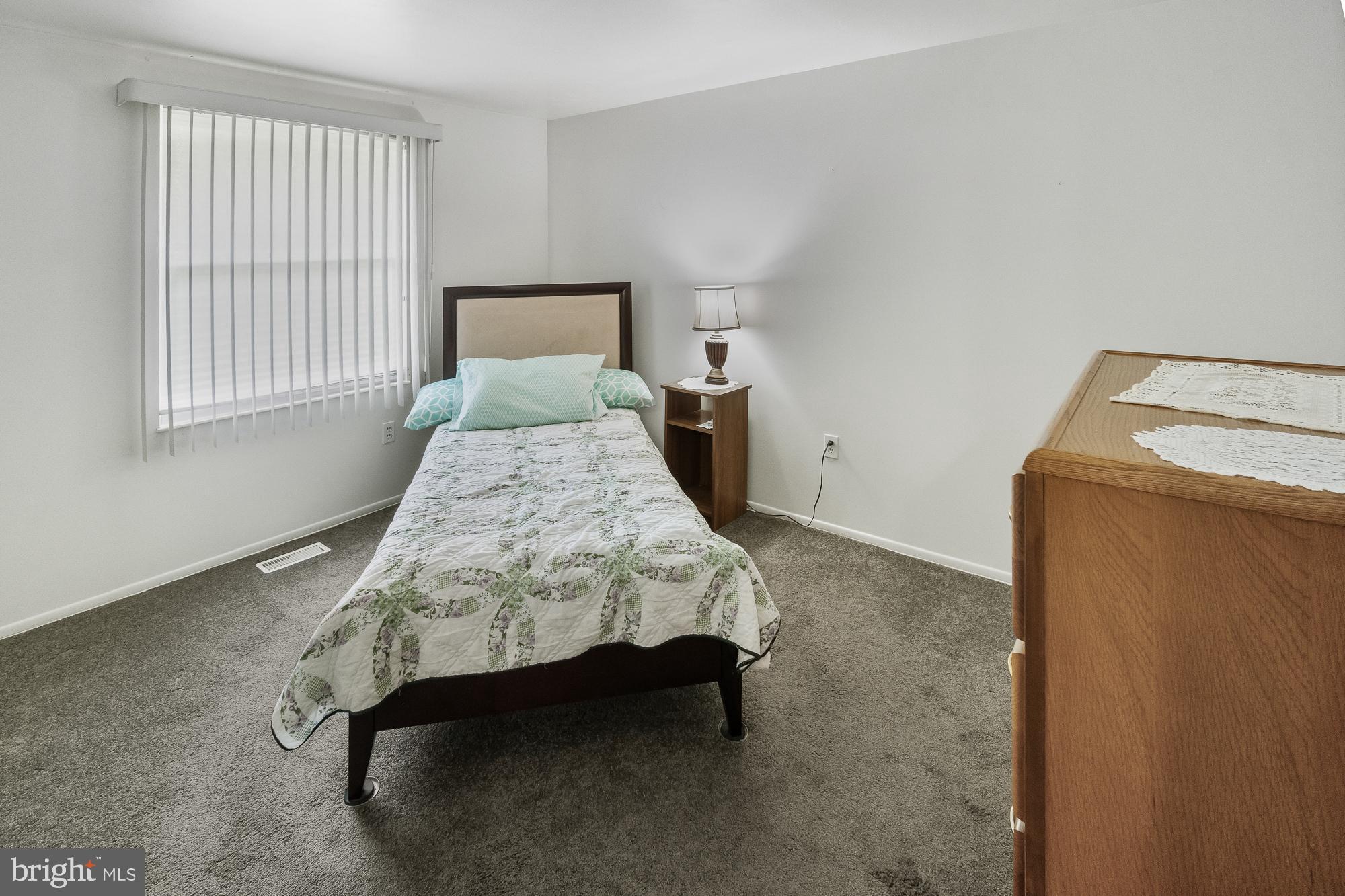 Bedroom with a single bed, patterned quilt, mint pillows, and wooden furniture.