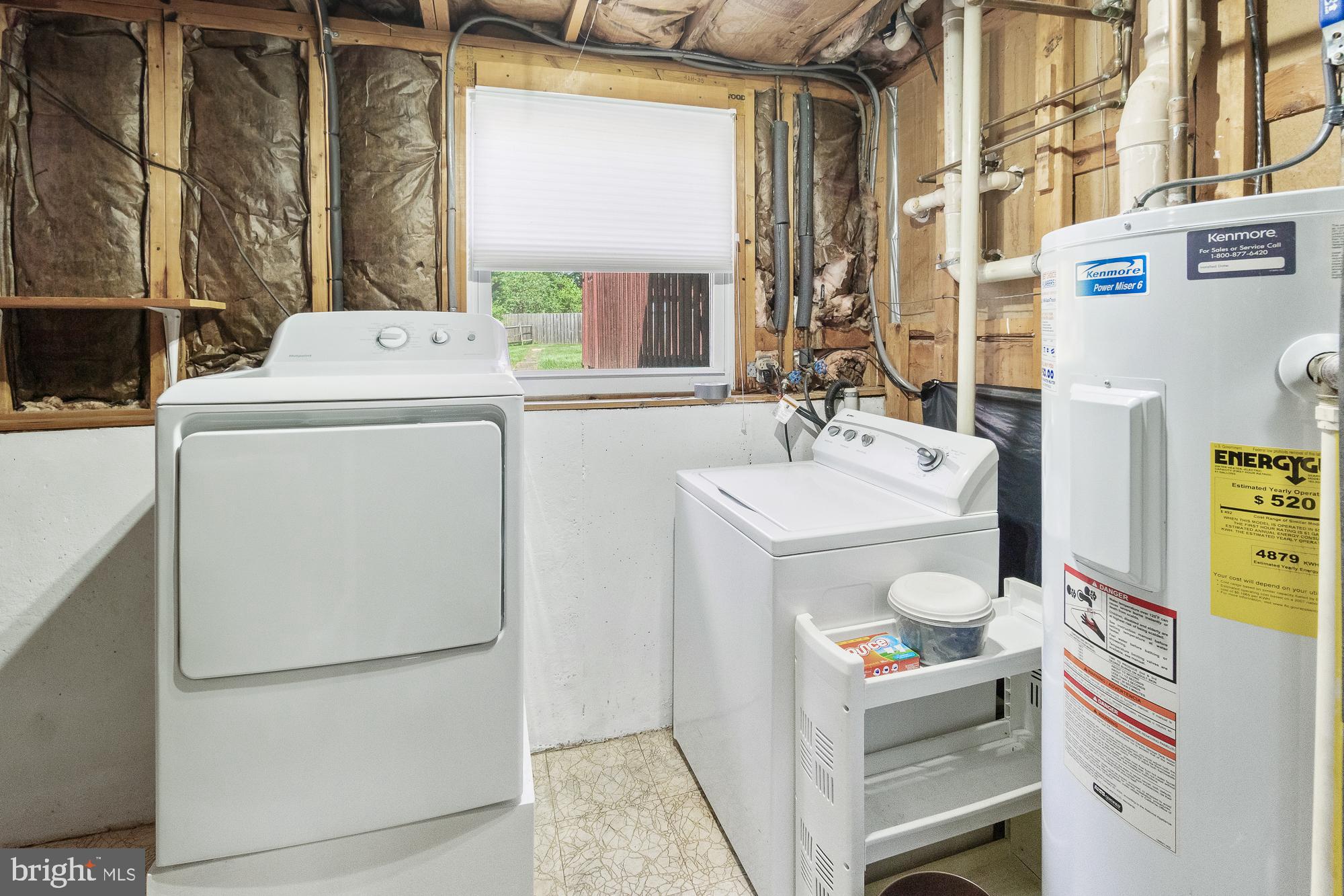 Laundry room with washer, dryer, and water heater; exposed framing and insulation line the walls.