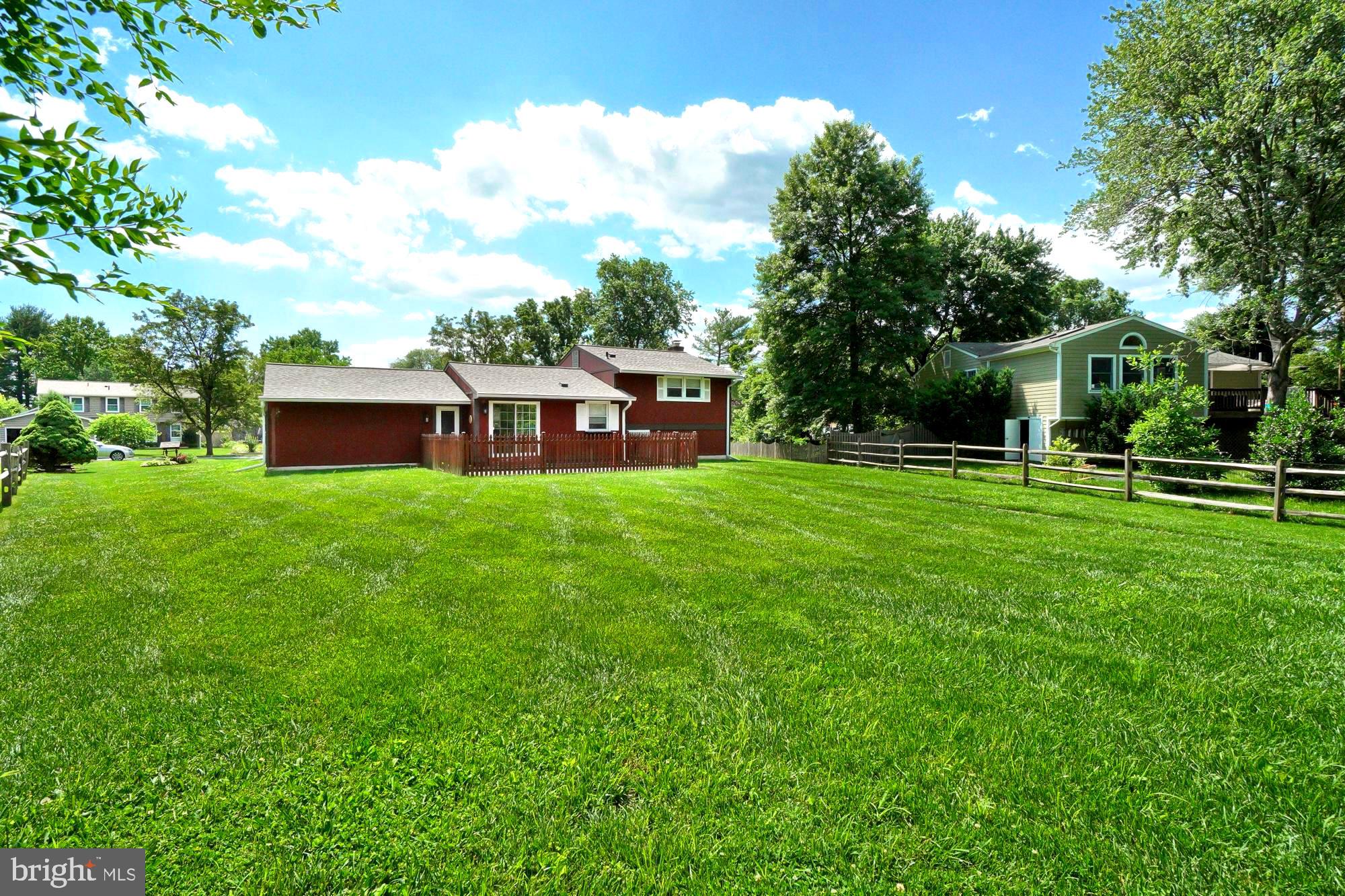 Red house’s rear exterior beyond a broad lawn, with a fenced patio and mature trees.