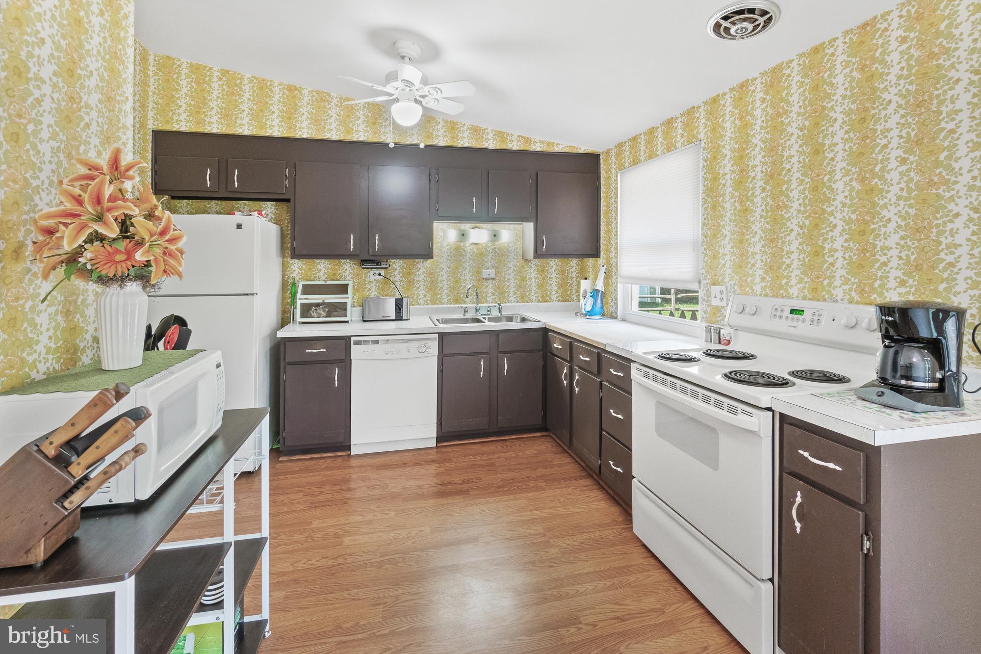 Kitchen with dark cabinets, yellow floral wallpaper, wood floors, and white appliances.