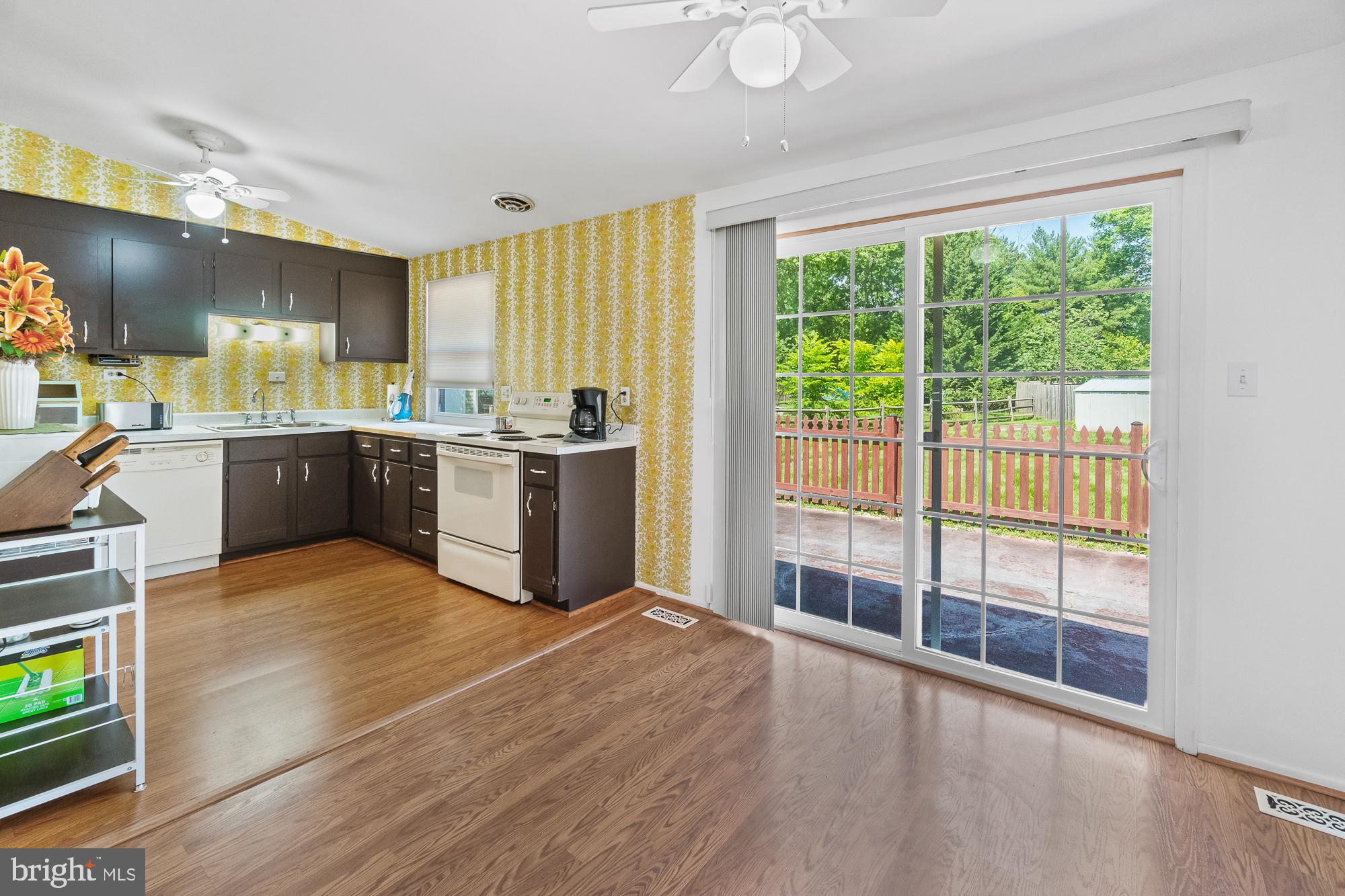 Kitchen with dark cabinets and yellow patterned wallpaper beside sliding doors to a deck.