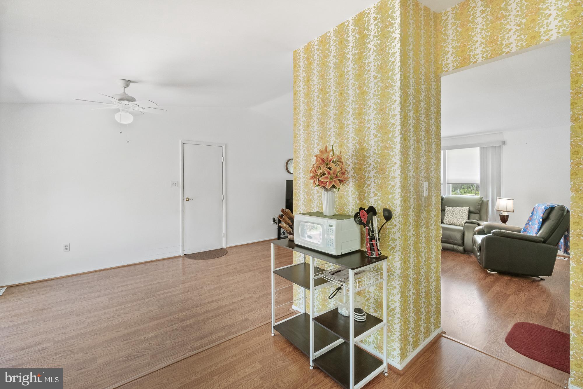 Open-plan interior with wood floors, a yellow floral partition, and an adjoining furnished living room.