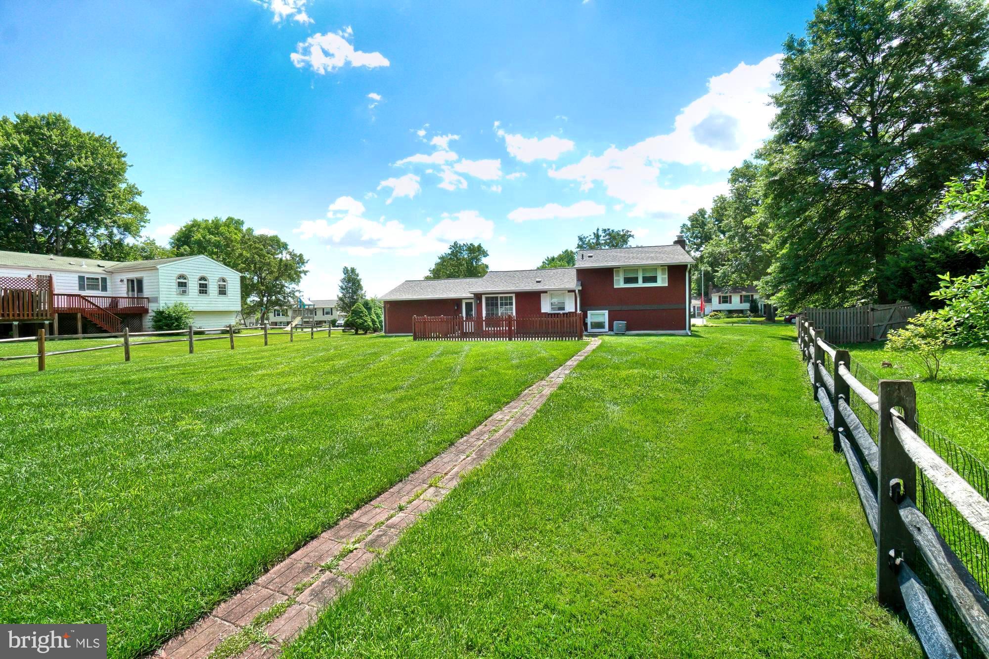 Red two-story home beyond a broad lawn, with a brick path and wooden fences.