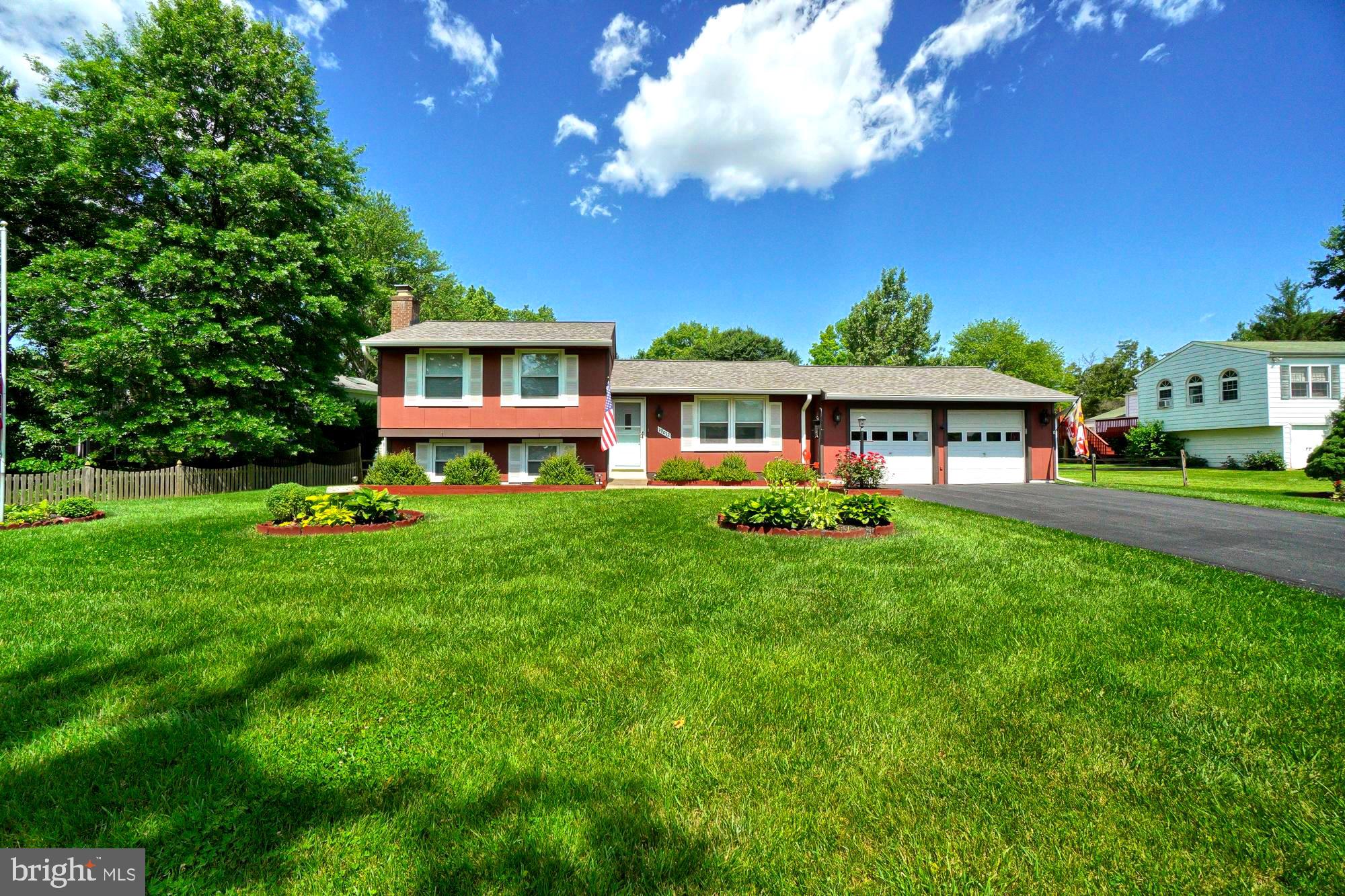 Red split-level home with a two-car garage, landscaped lawn, and mature trees.