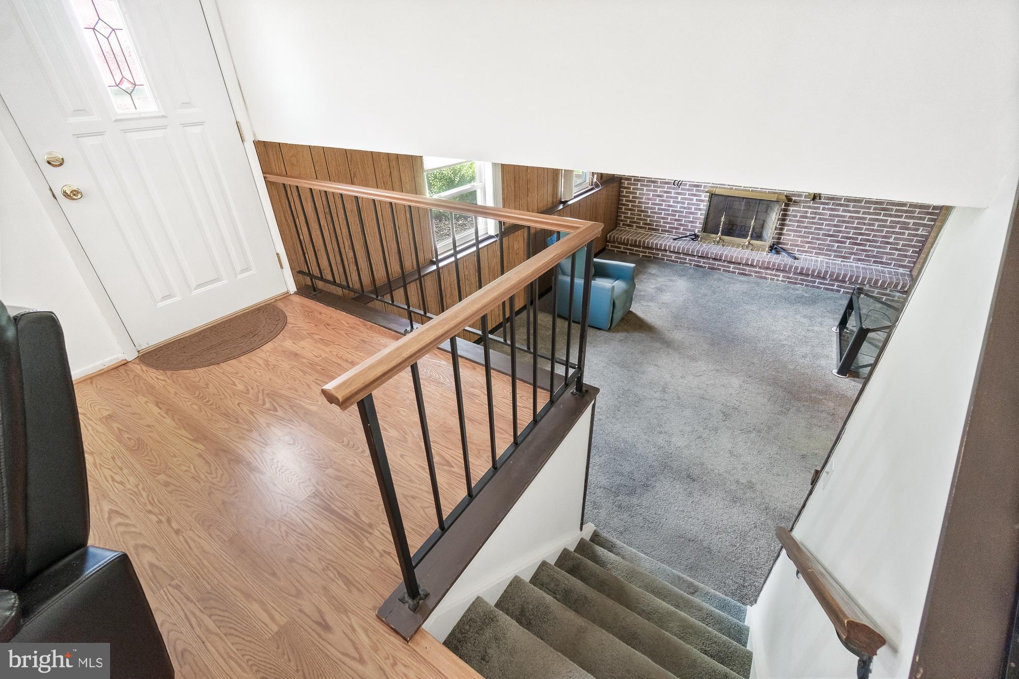 Entry foyer overlooking a carpeted living room with a brick fireplace and wood-topped railing.
