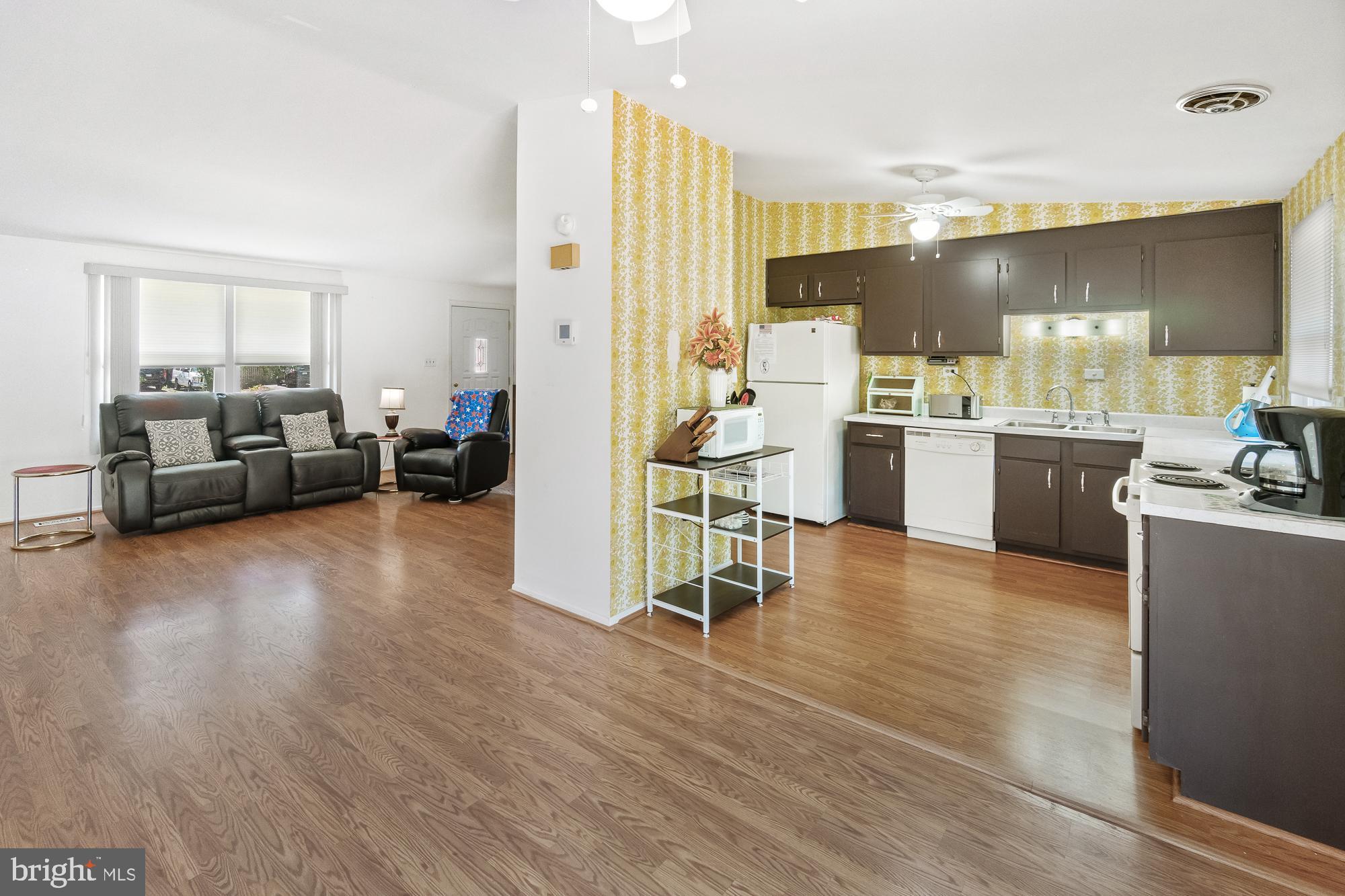 Open-plan living room and kitchen with dark cabinets, patterned yellow walls, and wood-look flooring.