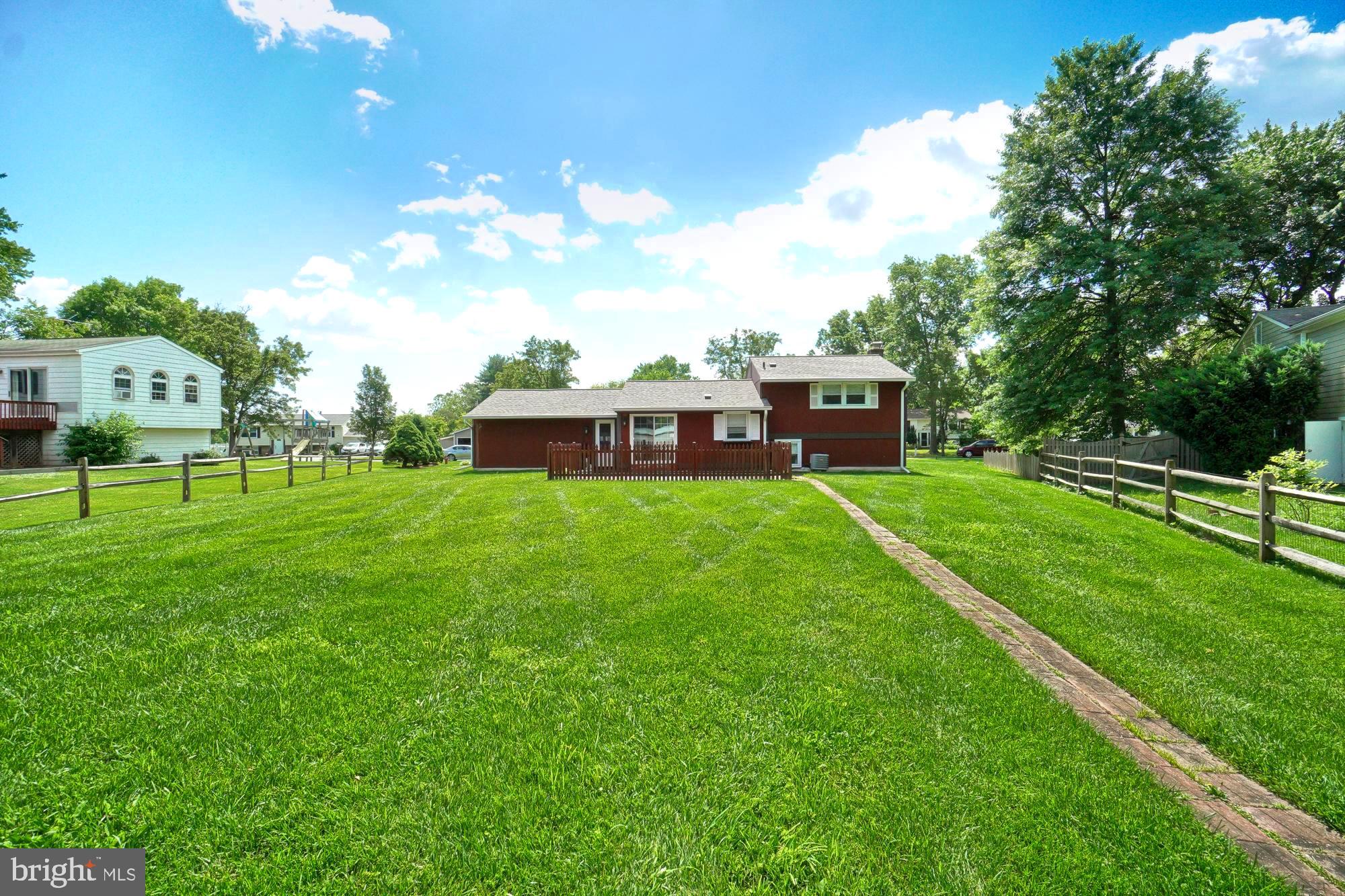 Rear of a red-brown split-level home beyond a broad lawn, with a brick path and fenced deck.