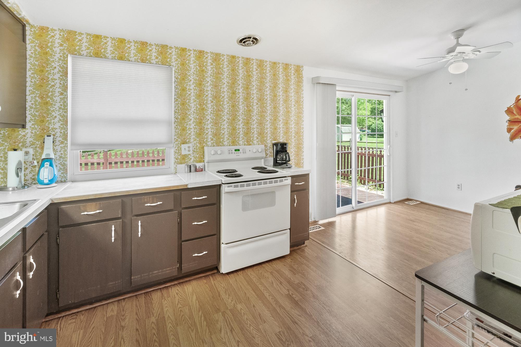Kitchen with yellow floral wallpaper, brown cabinets, and sliding glass doors to a fenced yard.