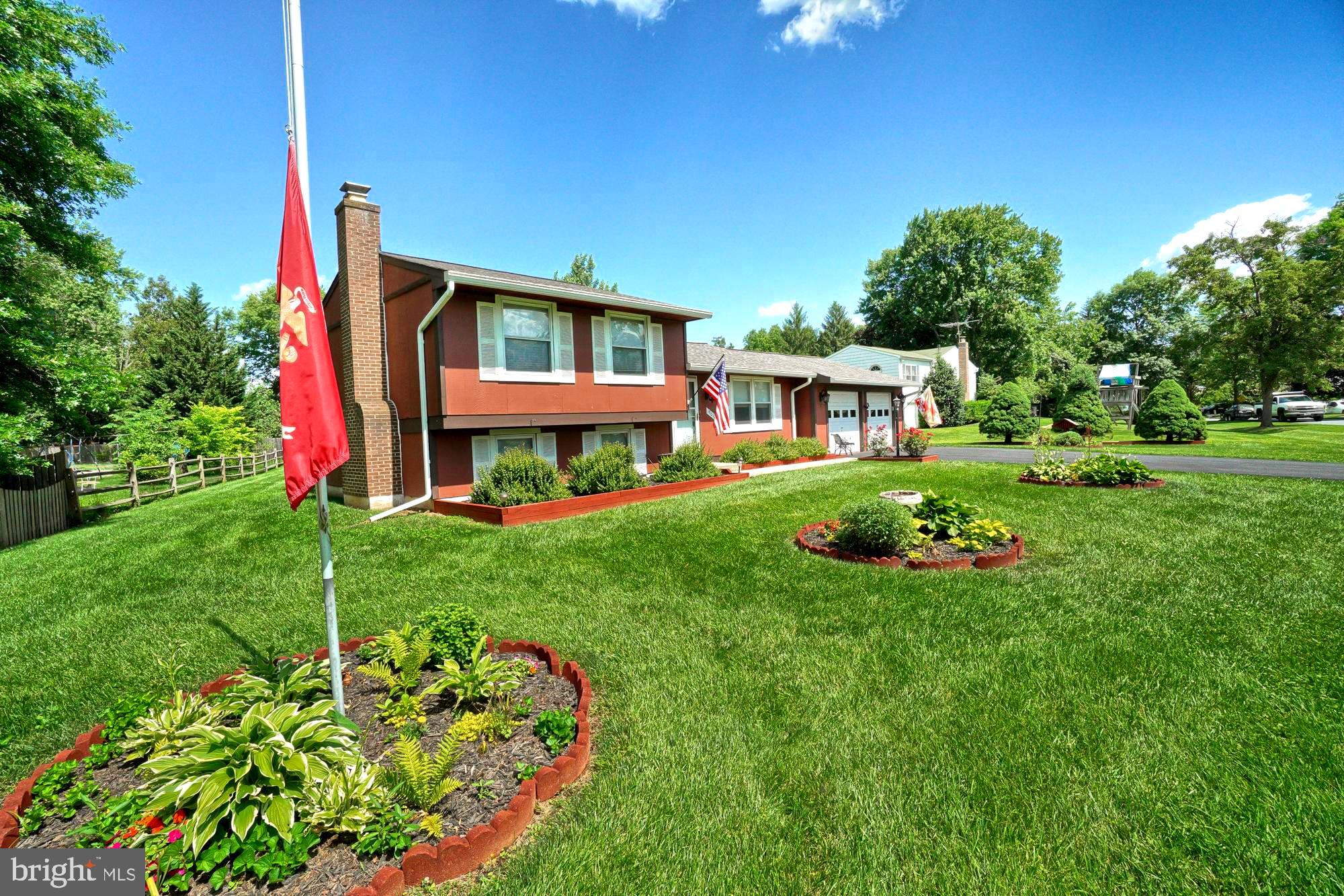 Red split-level house with an attached garage, landscaped beds, and a broad green lawn.