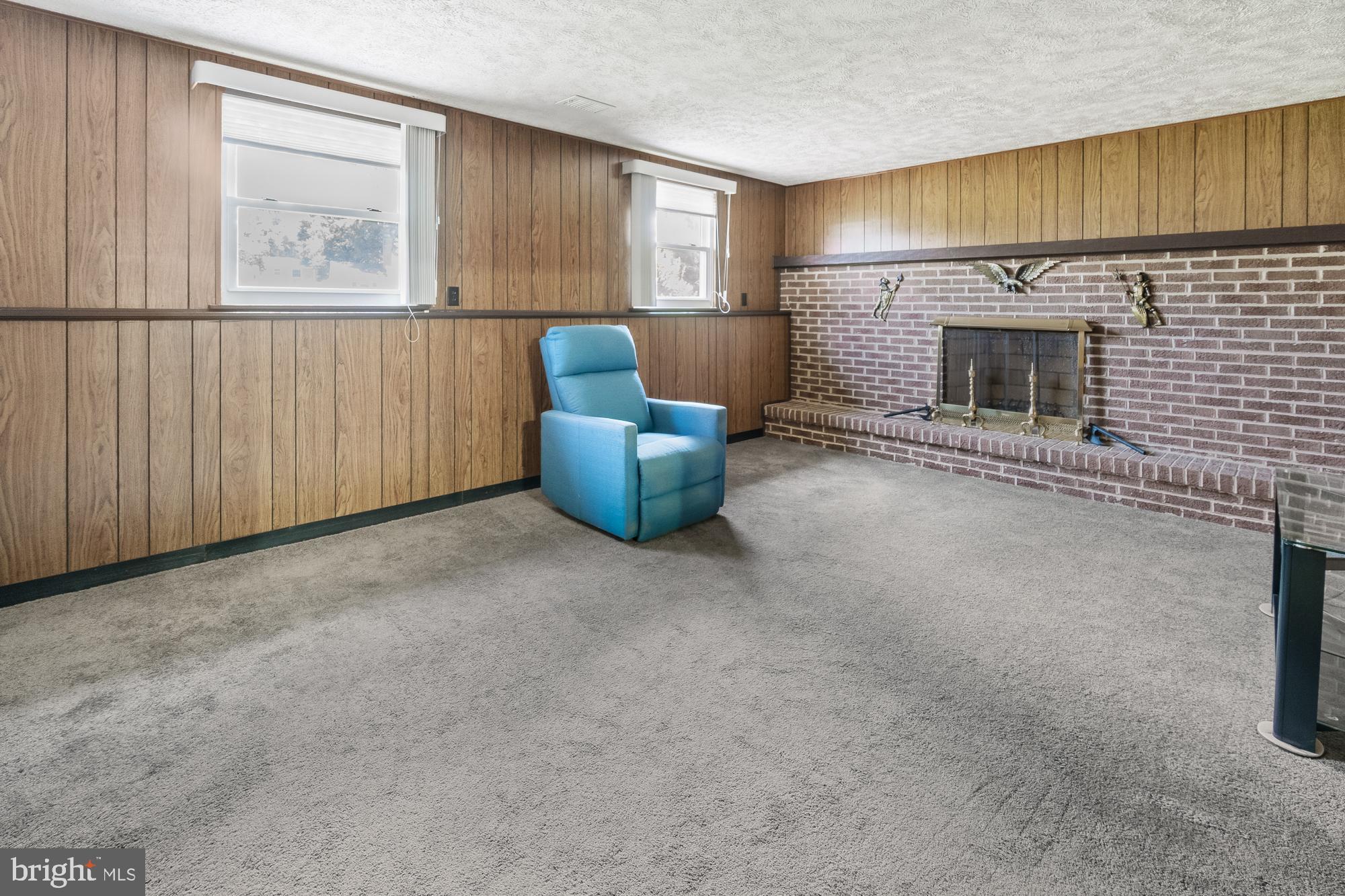 Carpeted room with wood-paneled walls, a brick fireplace, and a blue armchair.