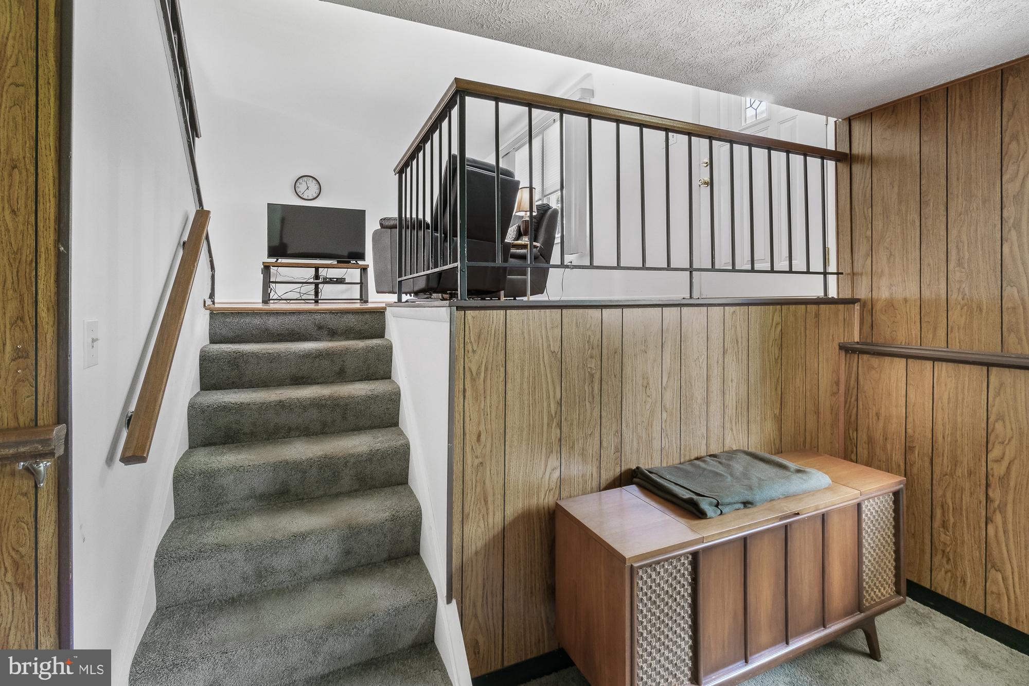 Carpeted stairs lead to an upper sitting area with a television, armchairs, and wood-paneled walls.