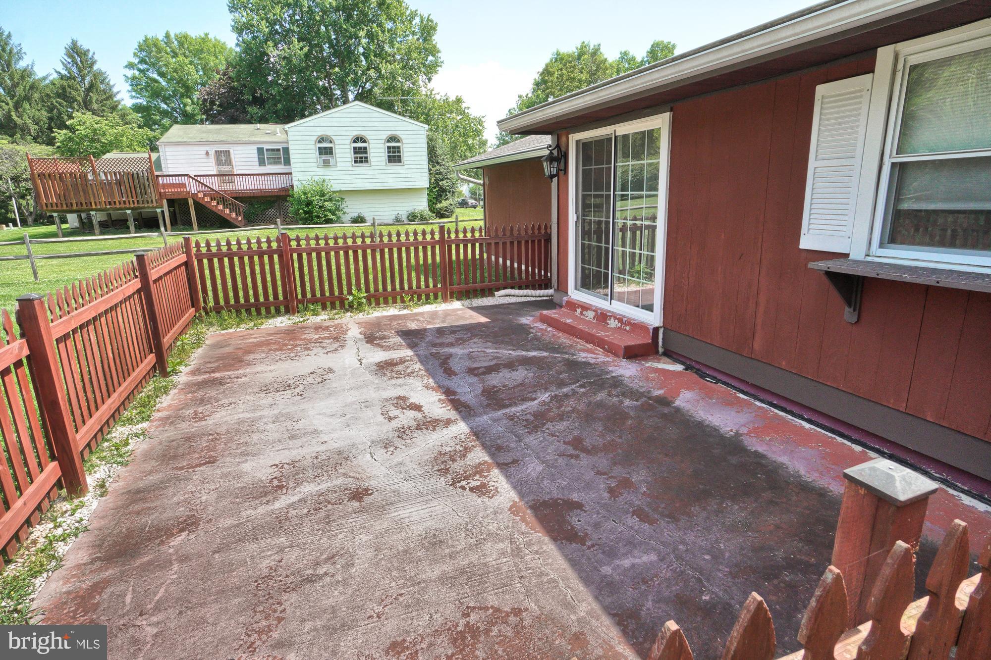 Concrete backyard patio beside a red-sided house, enclosed by a red picket fence.
