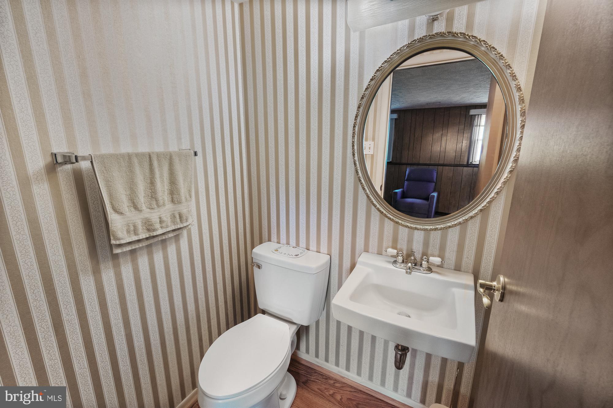 Small bathroom with striped wallpaper, pedestal sink, white toilet, and ornate oval mirror.