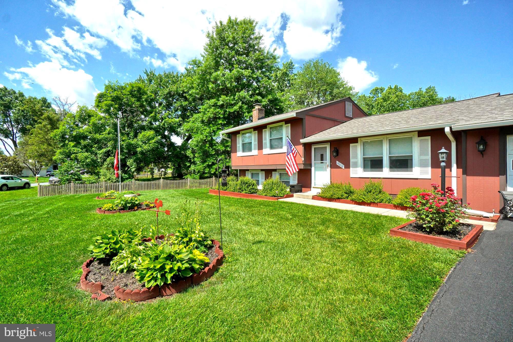 Red split-level home with white trim, landscaped flower beds, and a broad green lawn.