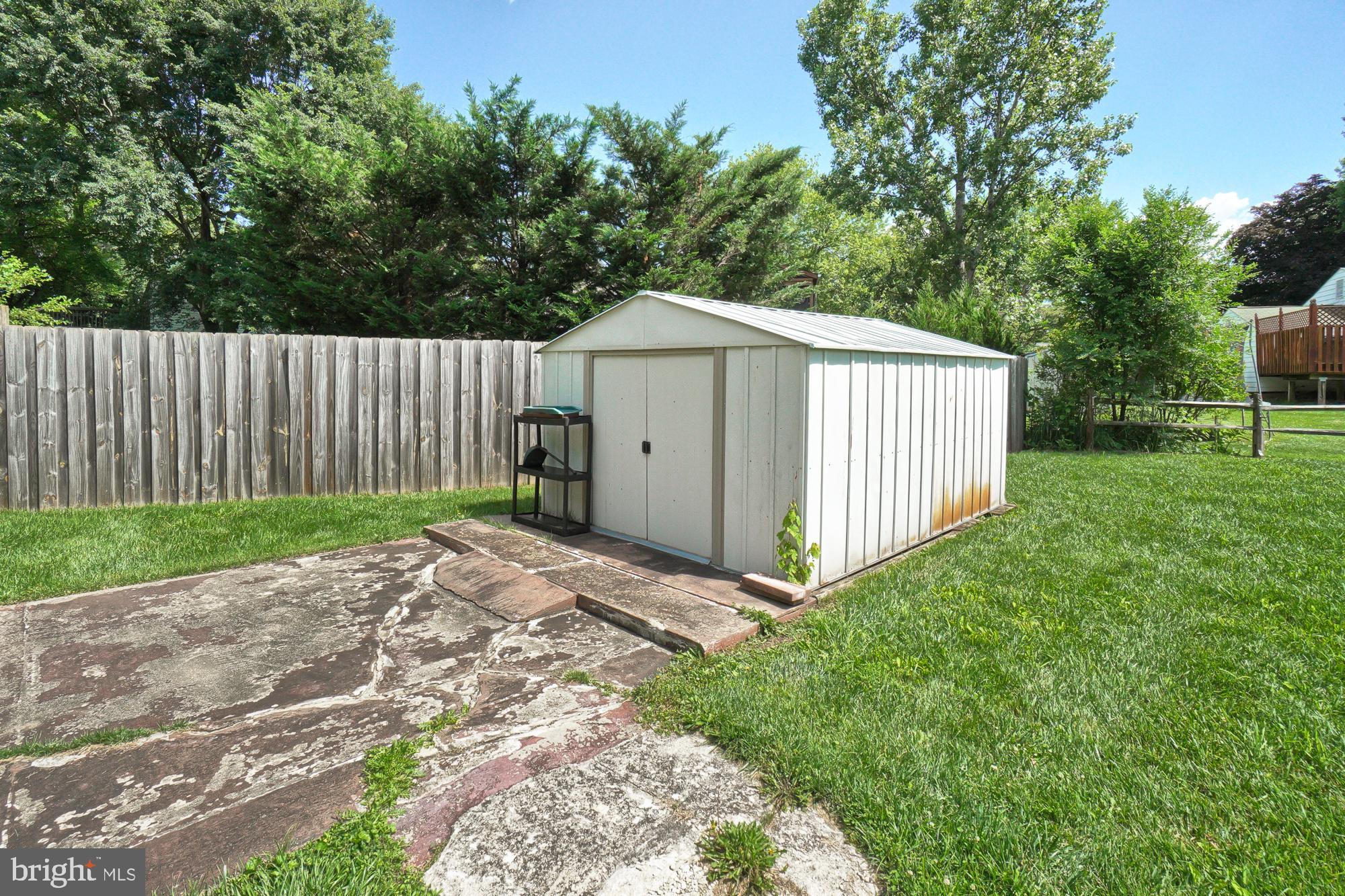 White metal storage shed in a fenced backyard beside a weathered concrete patio.