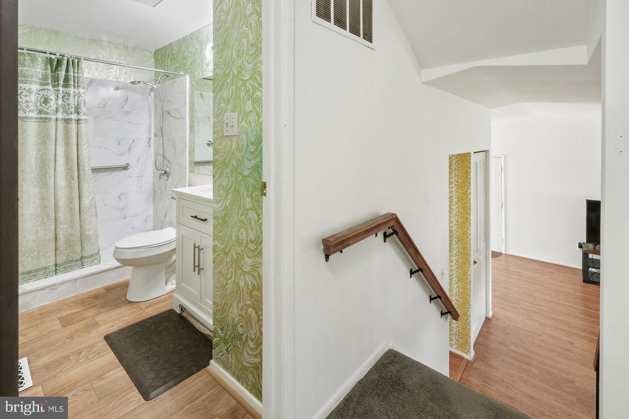 Bathroom with a marble-look shower beside a stair landing with a wooden handrail.