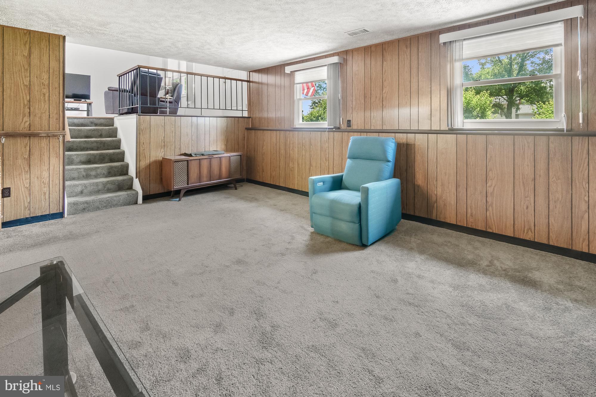 Carpeted living room with wood-paneled walls, a blue armchair, and stairs to an elevated seating area.