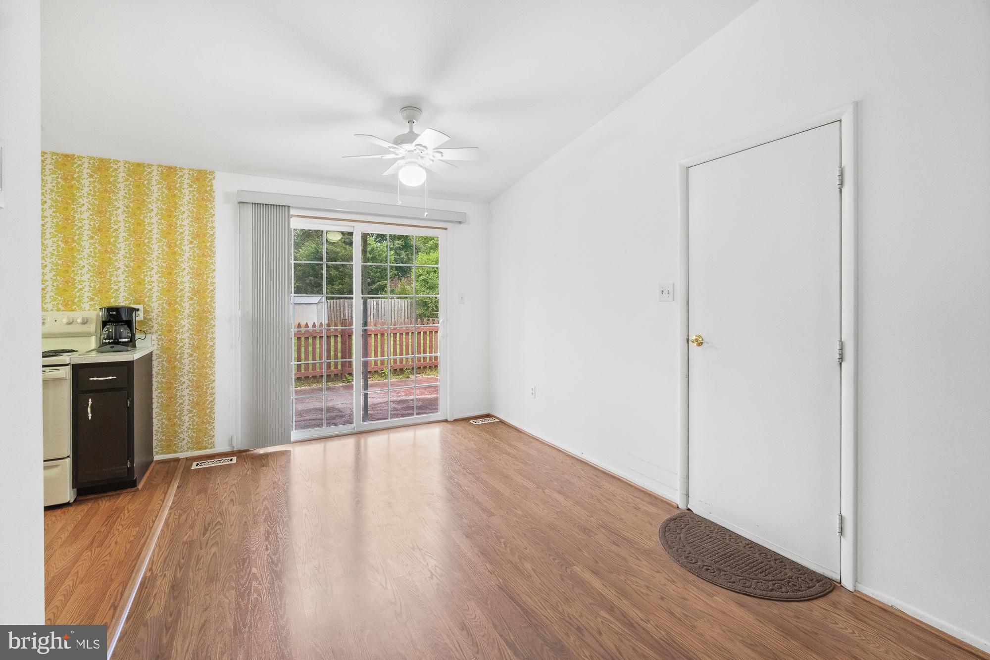 Dining area with wood-look flooring, yellow patterned wallpaper, and sliding glass doors to a fenced yard.