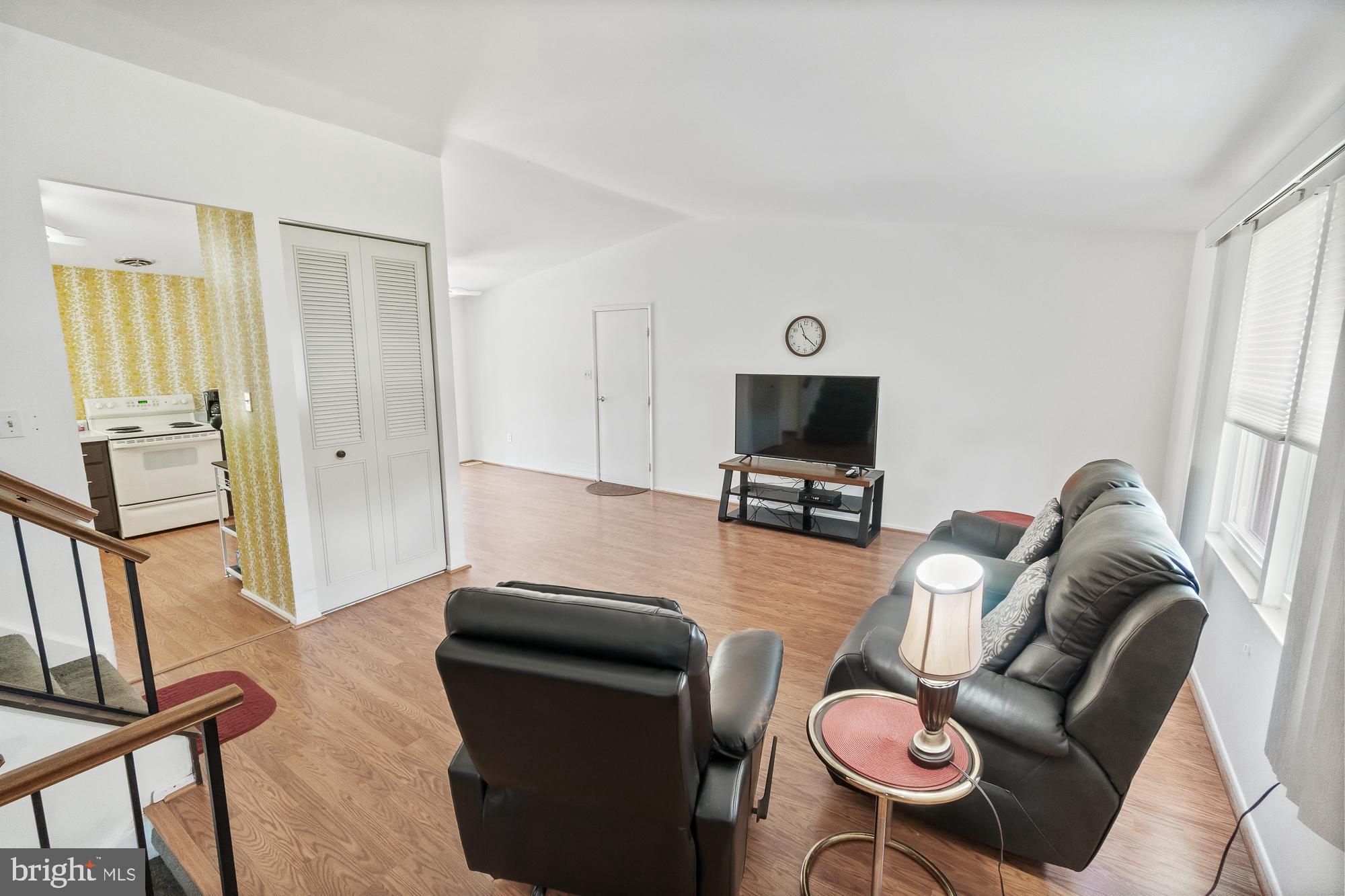 Living room with leather seating, wood floors, and large windows beside an open kitchen.