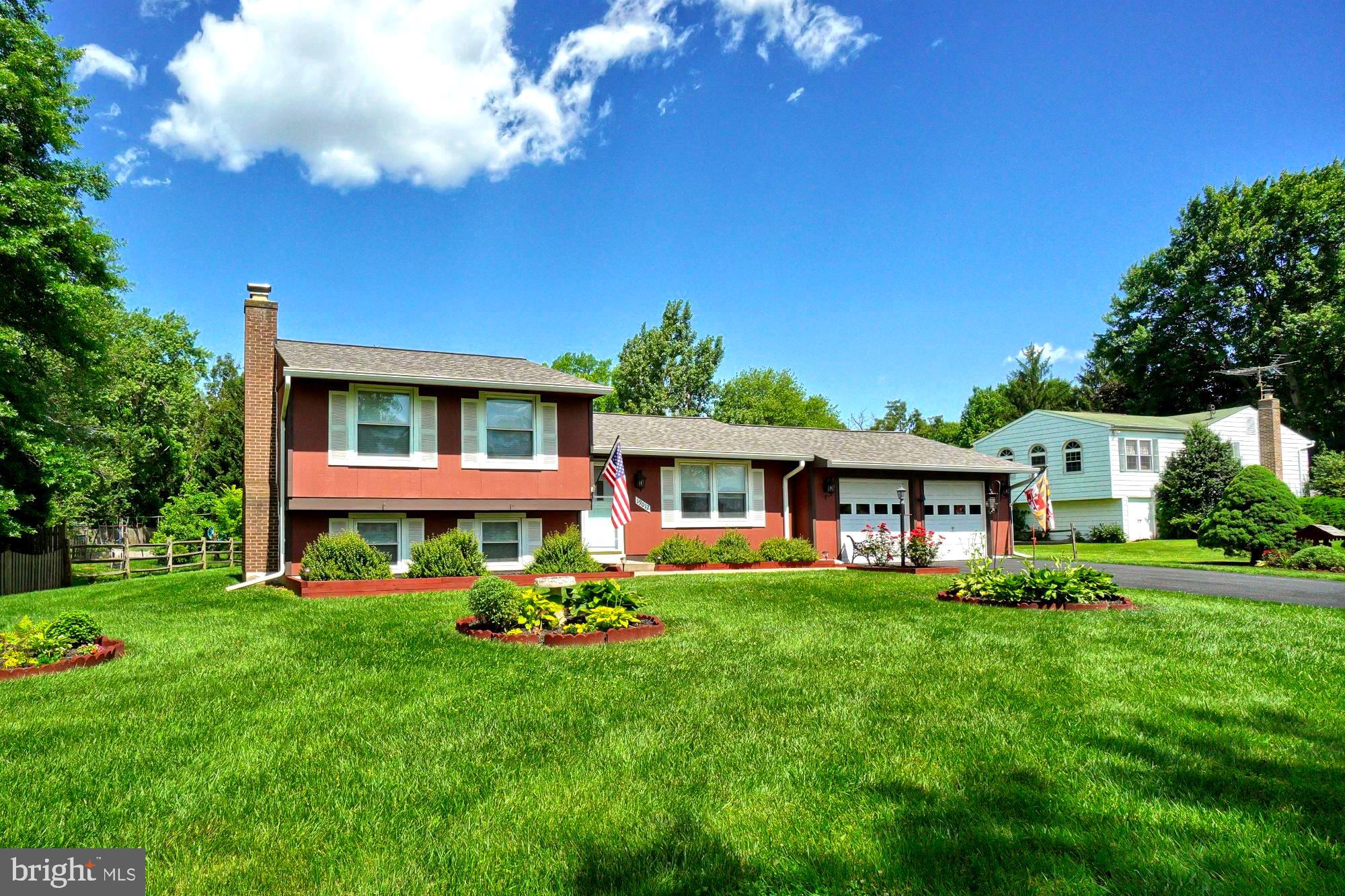 Reddish split-level home with a brick chimney, two-car garage, landscaped beds, and broad green lawn.