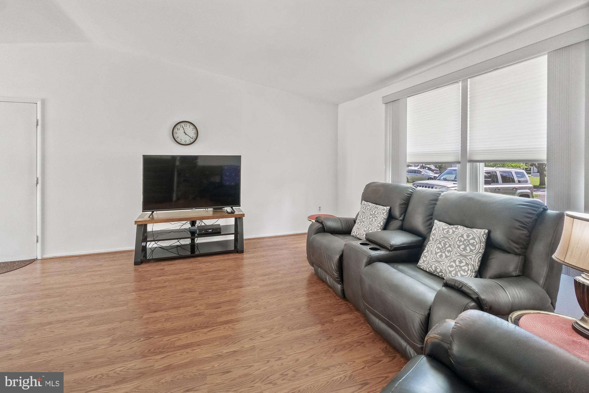 Living room with gray leather recliners, wood flooring, and a television beside large windows.