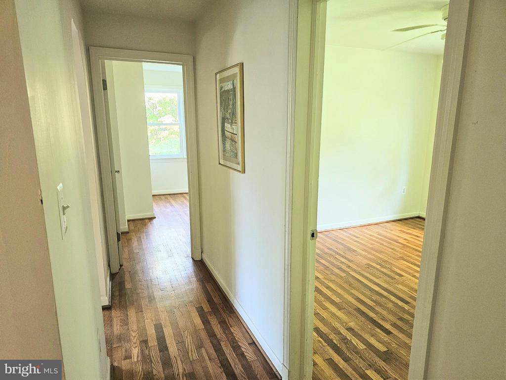 Hallway with hardwood floors and open doorways to two bright, empty rooms.