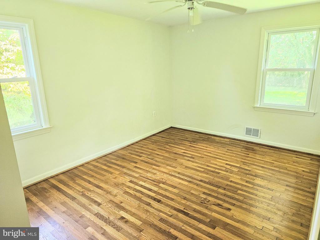 Empty bedroom with hardwood floors, two windows, and a ceiling fan.