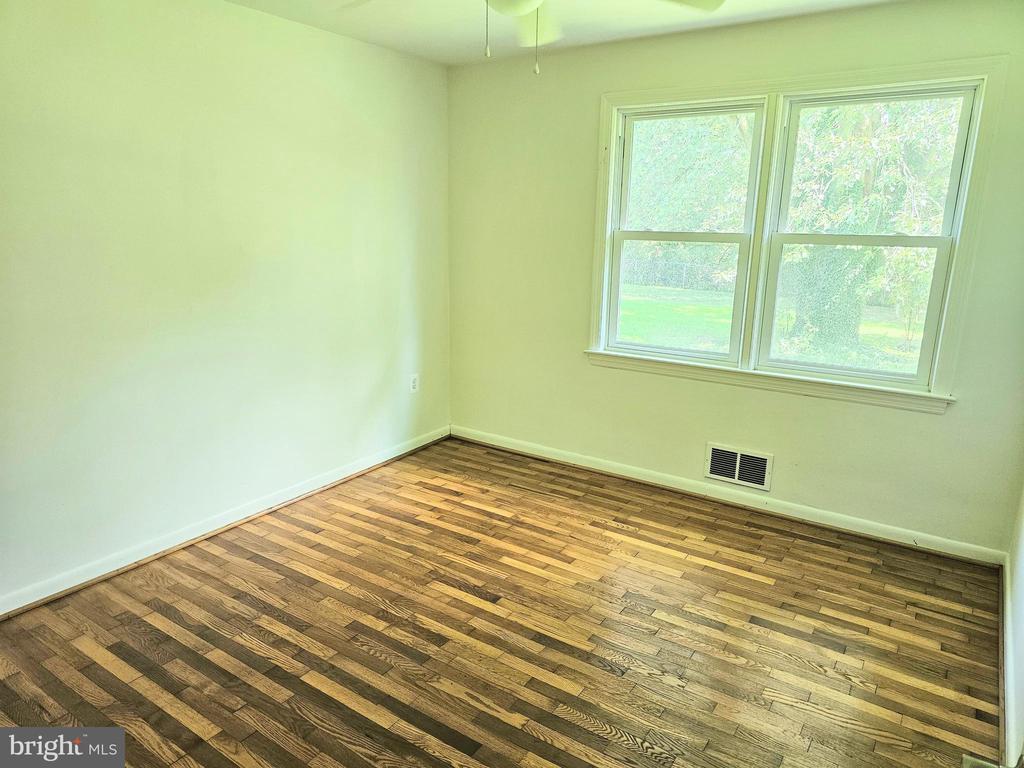Vacant room with hardwood floors and a double window overlooking greenery.