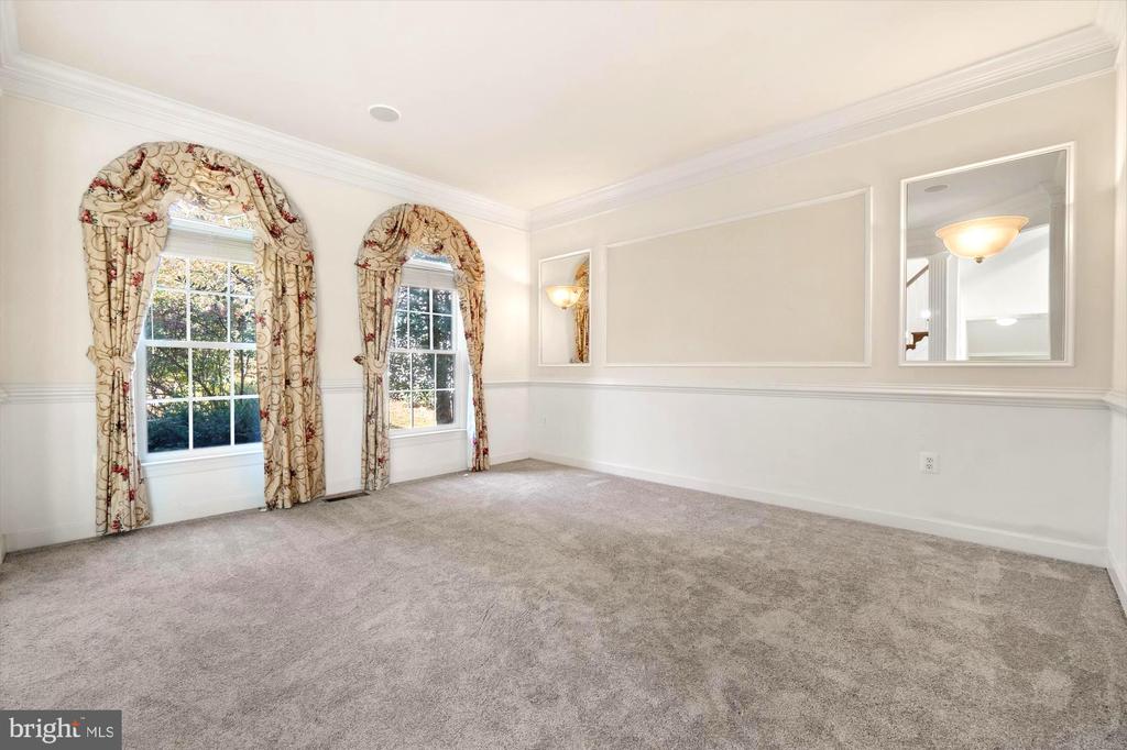 Vacant carpeted room with two tall curtained windows, decorative molding, and wall mirrors.