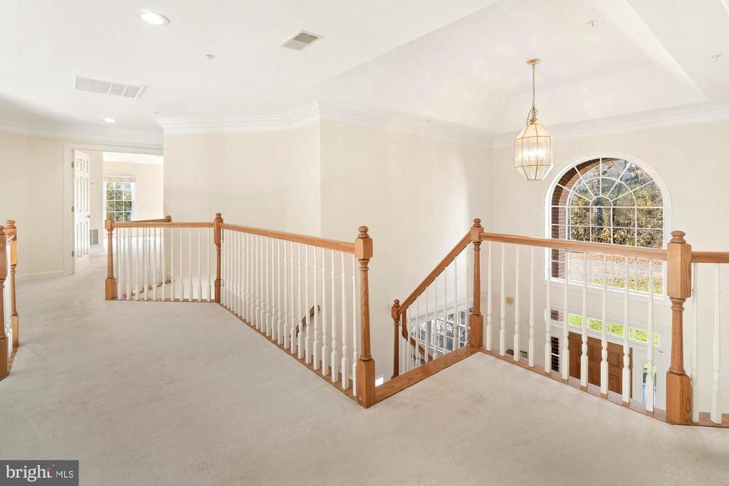 Upper-level landing overlooking the foyer, with wood-and-white railings and a large arched window.