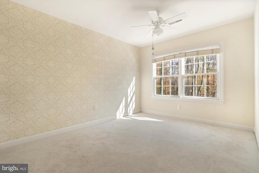 Empty bedroom with patterned wallpaper, a ceiling fan, and a large window overlooking trees.