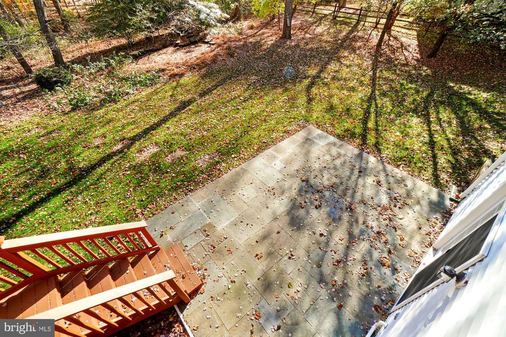 Stone patio and wooden deck steps overlook a wooded, leaf-covered backyard.