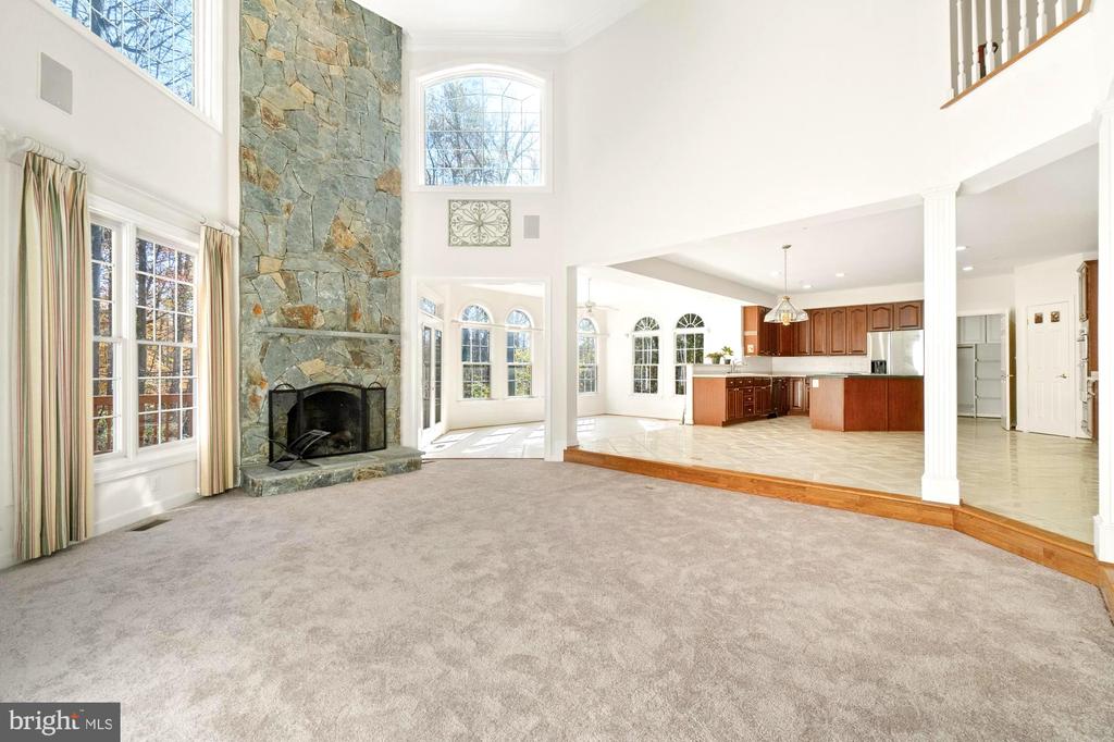 Two-story living room with a tall stone fireplace, large windows, and an open kitchen.