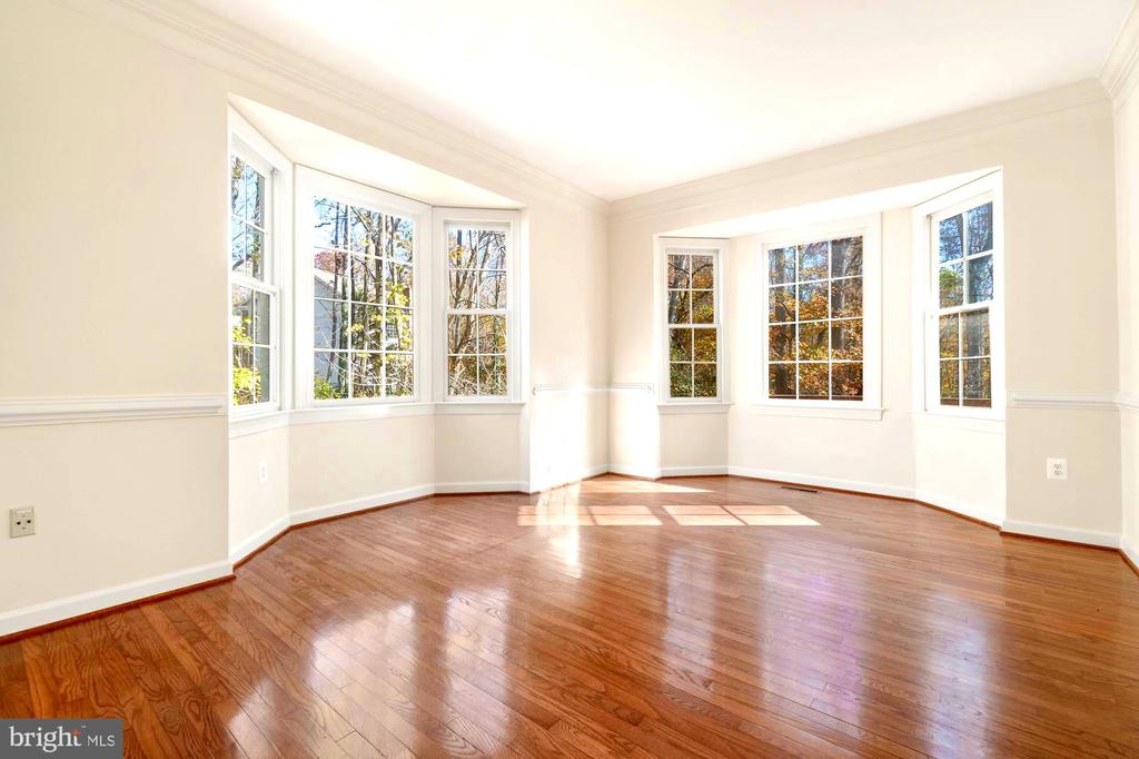 Empty room with polished hardwood floors and two large bay windows.