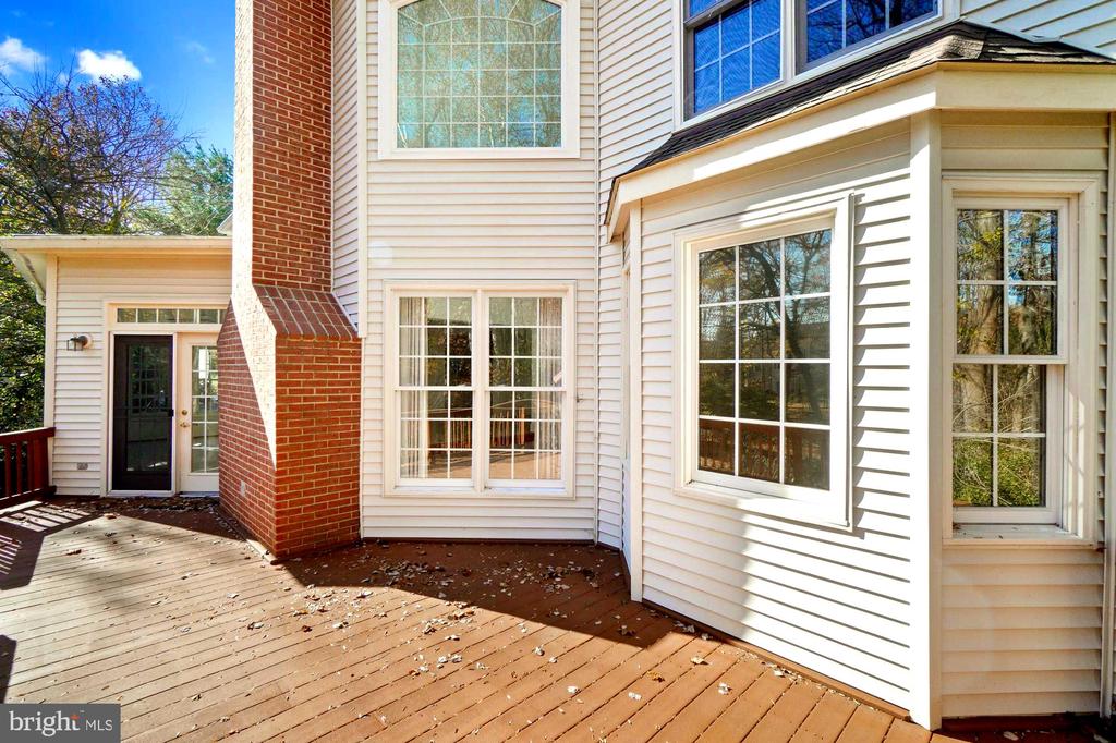 Rear of a light-sided house with a brick chimney and leaf-strewn wooden deck.