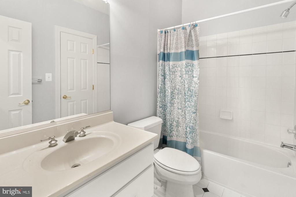 Bathroom with white vanity, toilet, and tub-shower behind a blue-and-white patterned curtain.