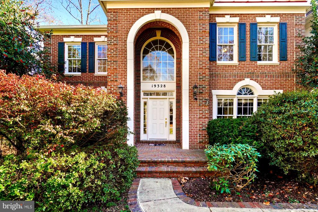 Red brick two-story home with blue shutters, an arched entry, and a curved front walkway.